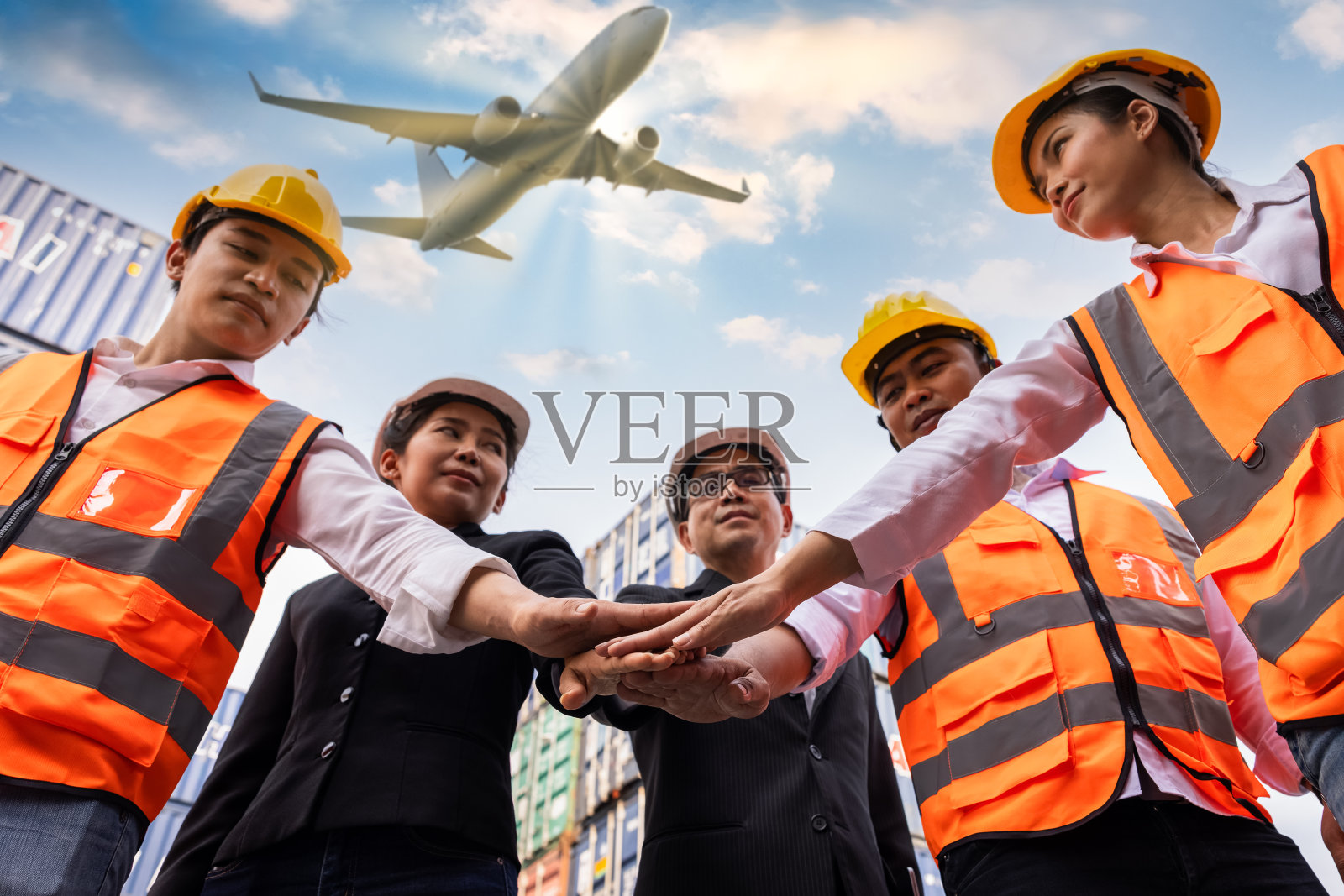 集团工程师和领班戴着安全帽站在集装箱现场，手拉着手货物，飞机背景角度，镜头选择性聚焦在手上。物流，团队合作和运输的概念。照片摄影图片