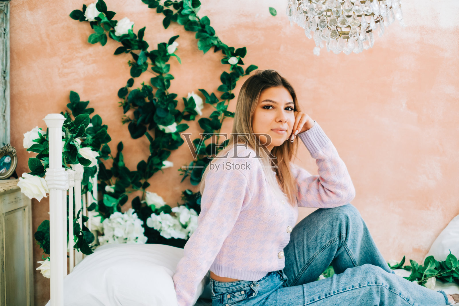 漂亮的白人女人坐在舒适明亮的卧室的床上，墙上挂着鲜花照片摄影图片