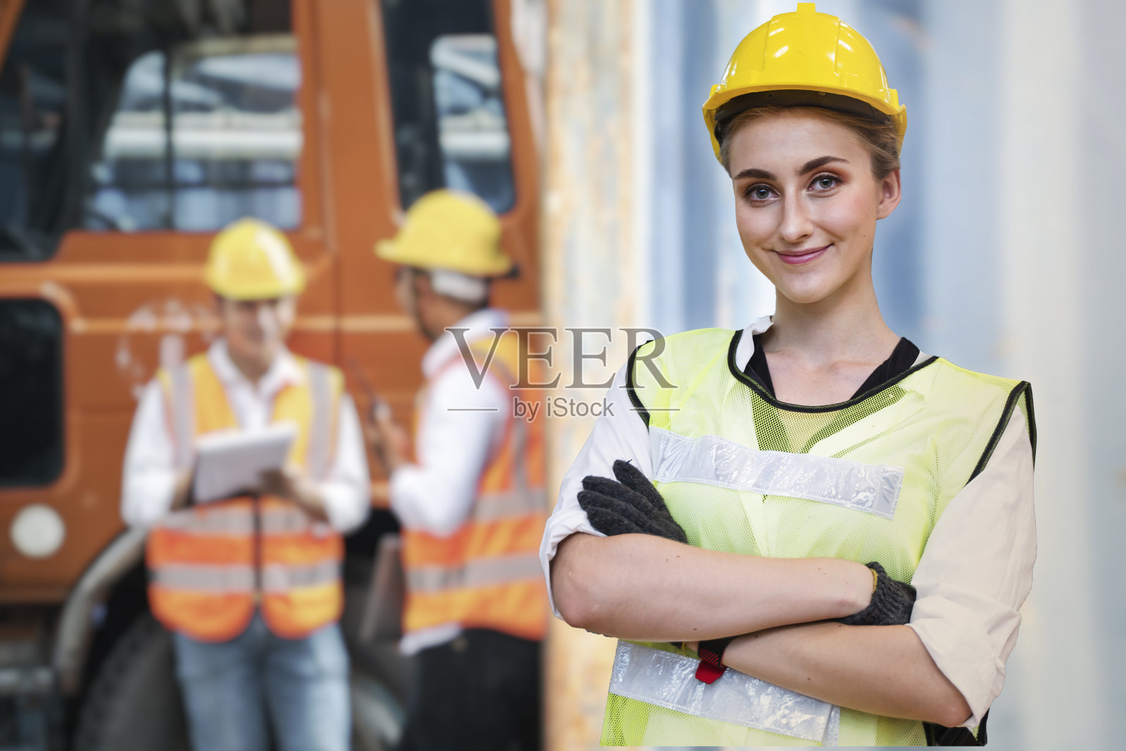 一位身穿蓝色工作服、头戴安全帽的女工程师自信地站在正在重型机械车辆前检查和开会的工人面前。照片摄影图片