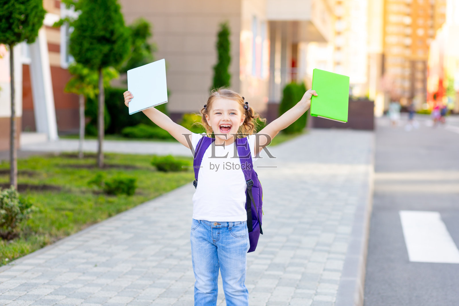 回到学校，一个快乐的女生背着书包，手里拿着课本，正准备上小学一年级，大喊着万岁照片摄影图片