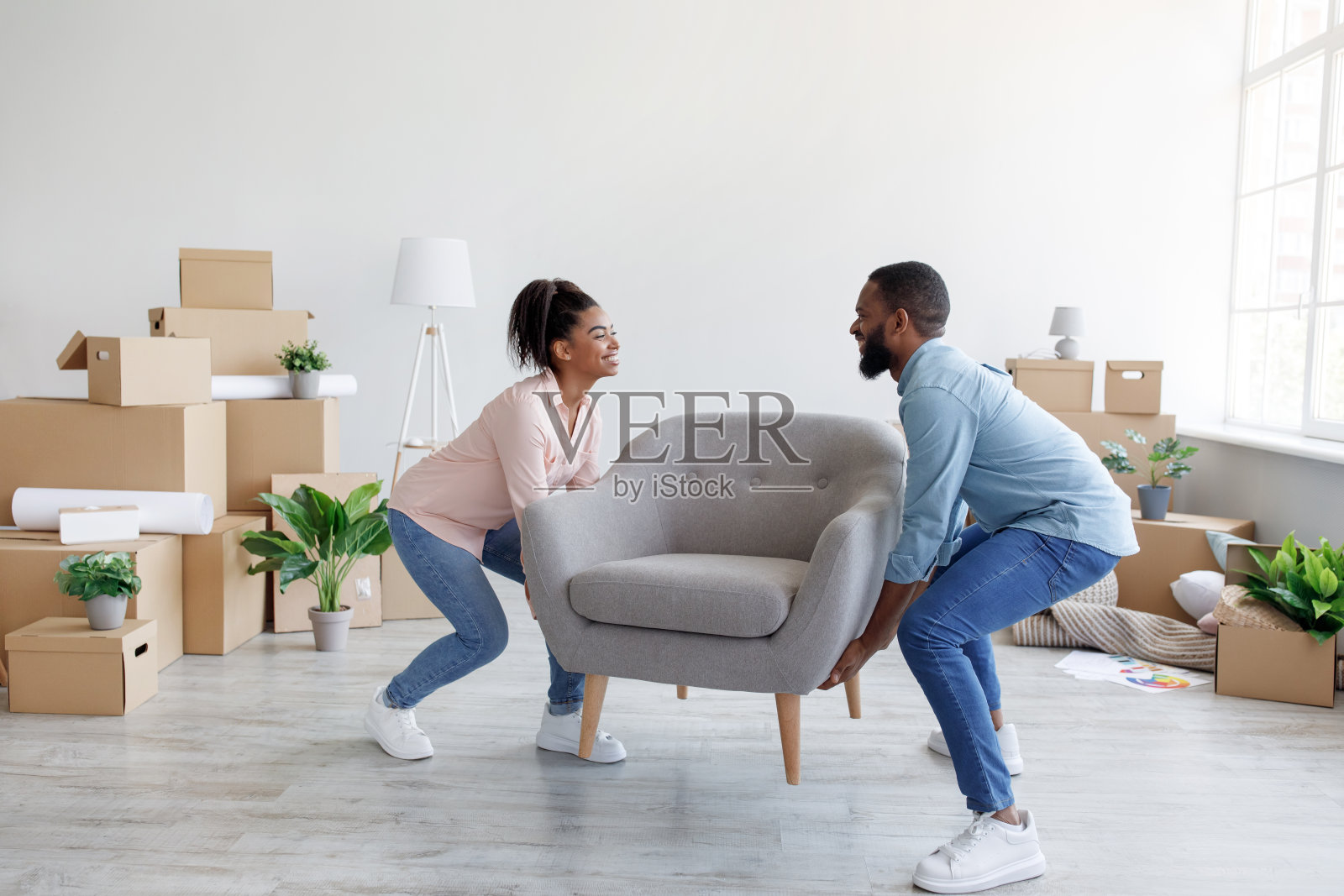 开朗的年轻黑人男女搬着扶手椅到新公寓，里面装着纸箱照片摄影图片