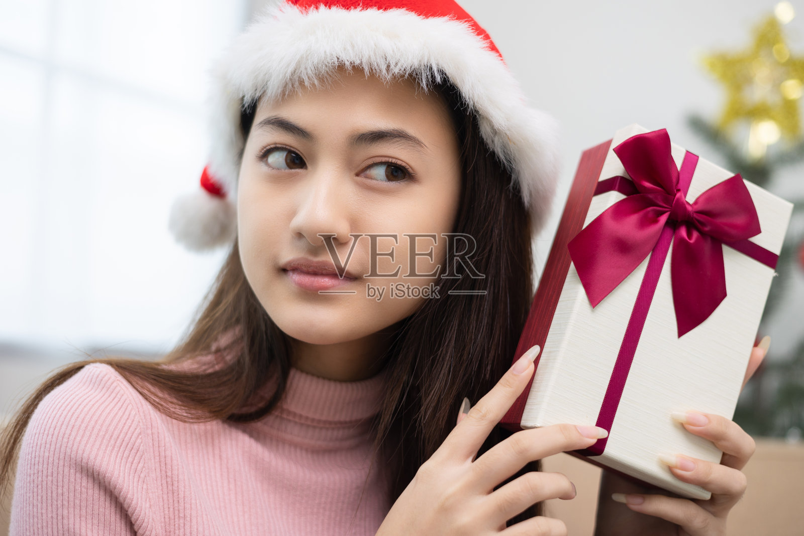 漂亮的亚洲女人拿着礼物盒猜猜盒子里有什么。年轻快乐可爱的小女孩在圣诞节节日里拿着许多礼品盒坐在家里的沙发上庆祝照片摄影图片