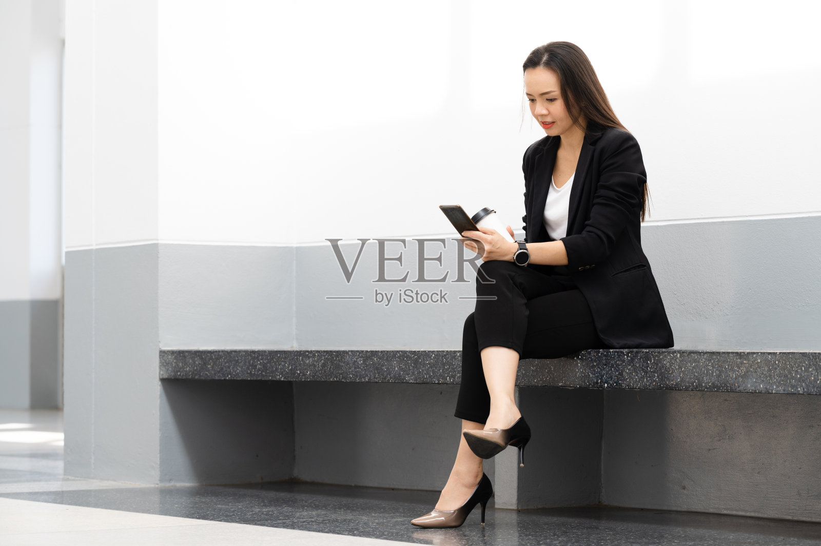 一位中年亚洲女商人拿着手机，拿着咖啡，对着镜头微笑照片摄影图片