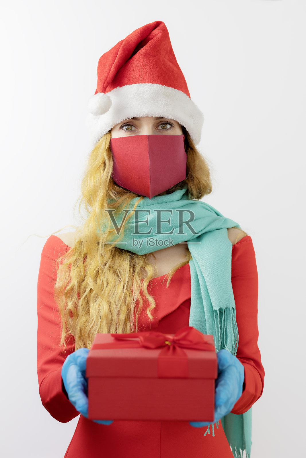 戴着防护面具和手套的圣诞老人夫人拿着一个装着礼物的盒子。无菌的礼物。受保护的圣诞节照片摄影图片