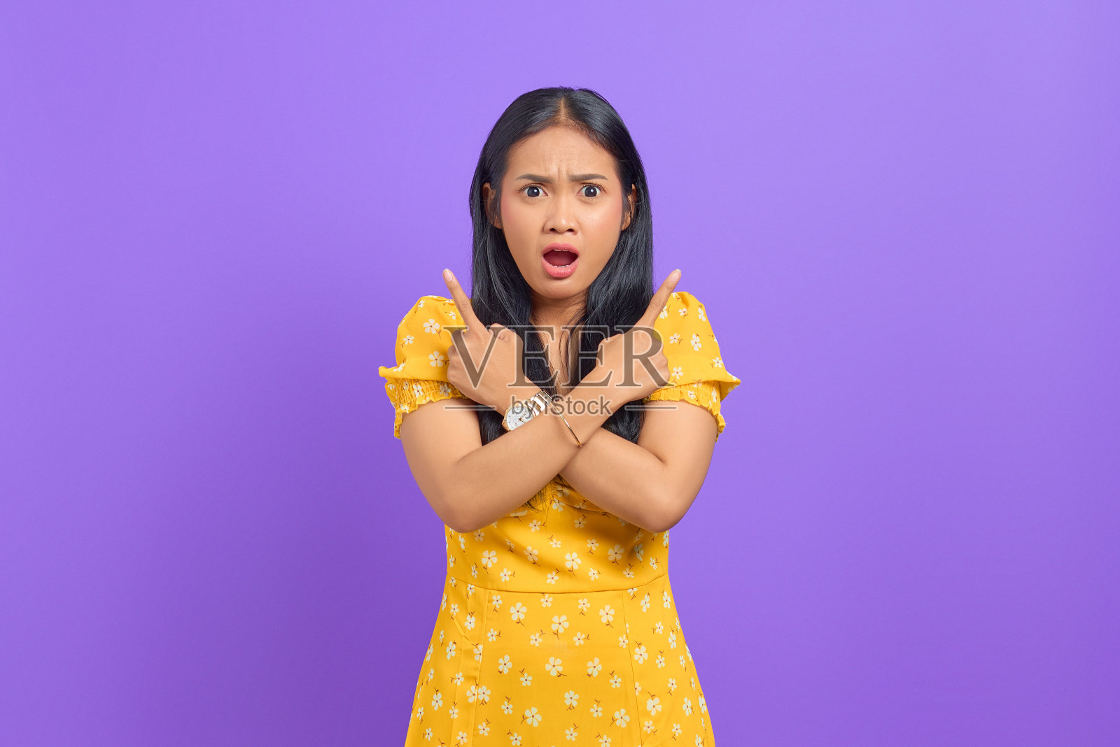 震惊的年轻亚洲女子指着一边，看着紫色背景下的相机照片摄影图片