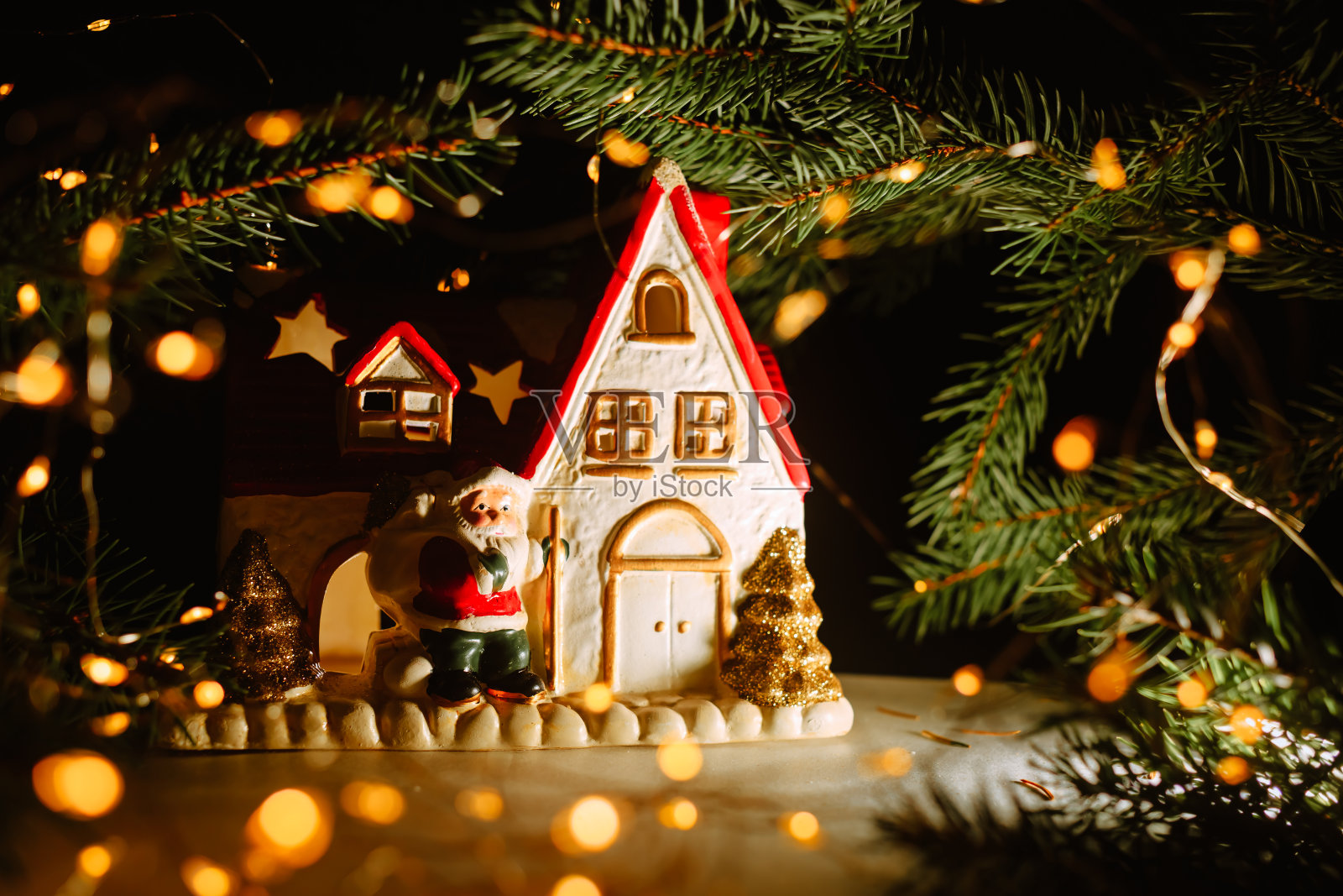 白色的房子，圣诞老人在一个模糊的黑暗的背景下，金色的散景和金色的花环。圣诞烛台。副本的空间。舒适的穿戴装饰项目。2021年新年大甩卖照片摄影图片