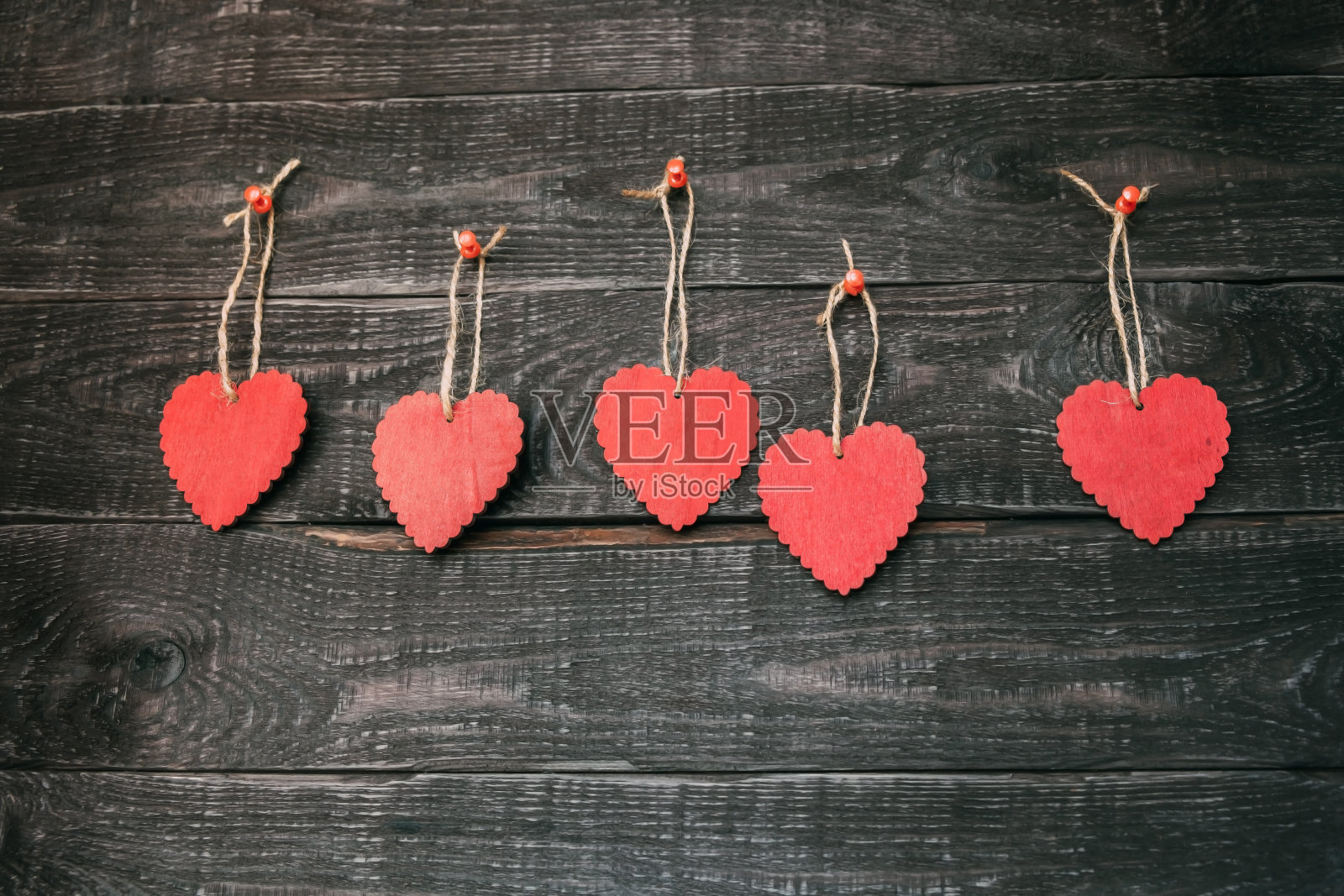 五颗木制的红心挂在绳子上，背景是深色的木头。照片摄影图片