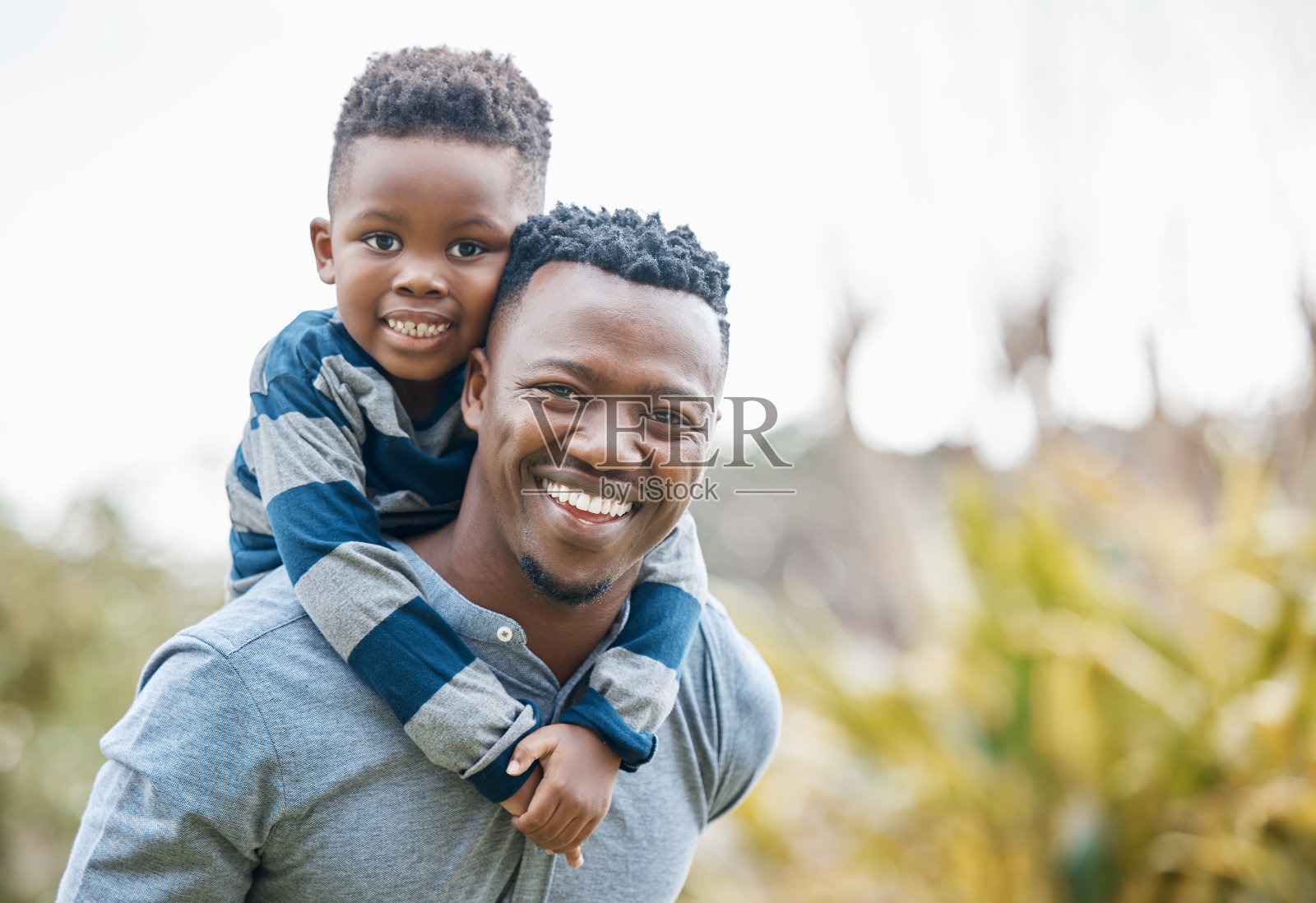 一个年轻的父亲和他的儿子在花园里骑在他背上照片摄影图片