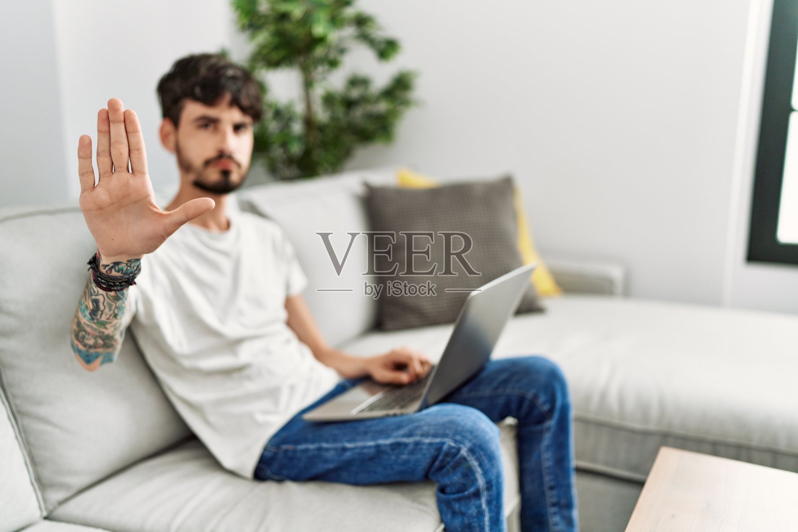 有胡子的西班牙男人坐在沙发上用手掌唱《停止歌唱》。面部带有否定和严肃的警告表情。照片摄影图片