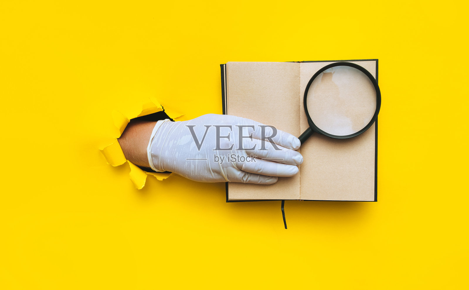 医生的手戴着白色乳胶医用手套，手里拿着一个放大镜，放在黄色背景的记事本上。有复印空间的破纸。有选择性的重点。搜索，缩放和研究概念。照片摄影图片