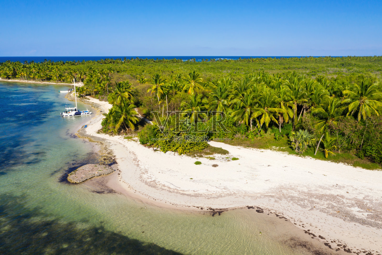 在加勒比海附近，一艘快艇沿着棕榈树环绕的热带岛屿漂浮。多米尼加共和国。鸟瞰图照片摄影图片
