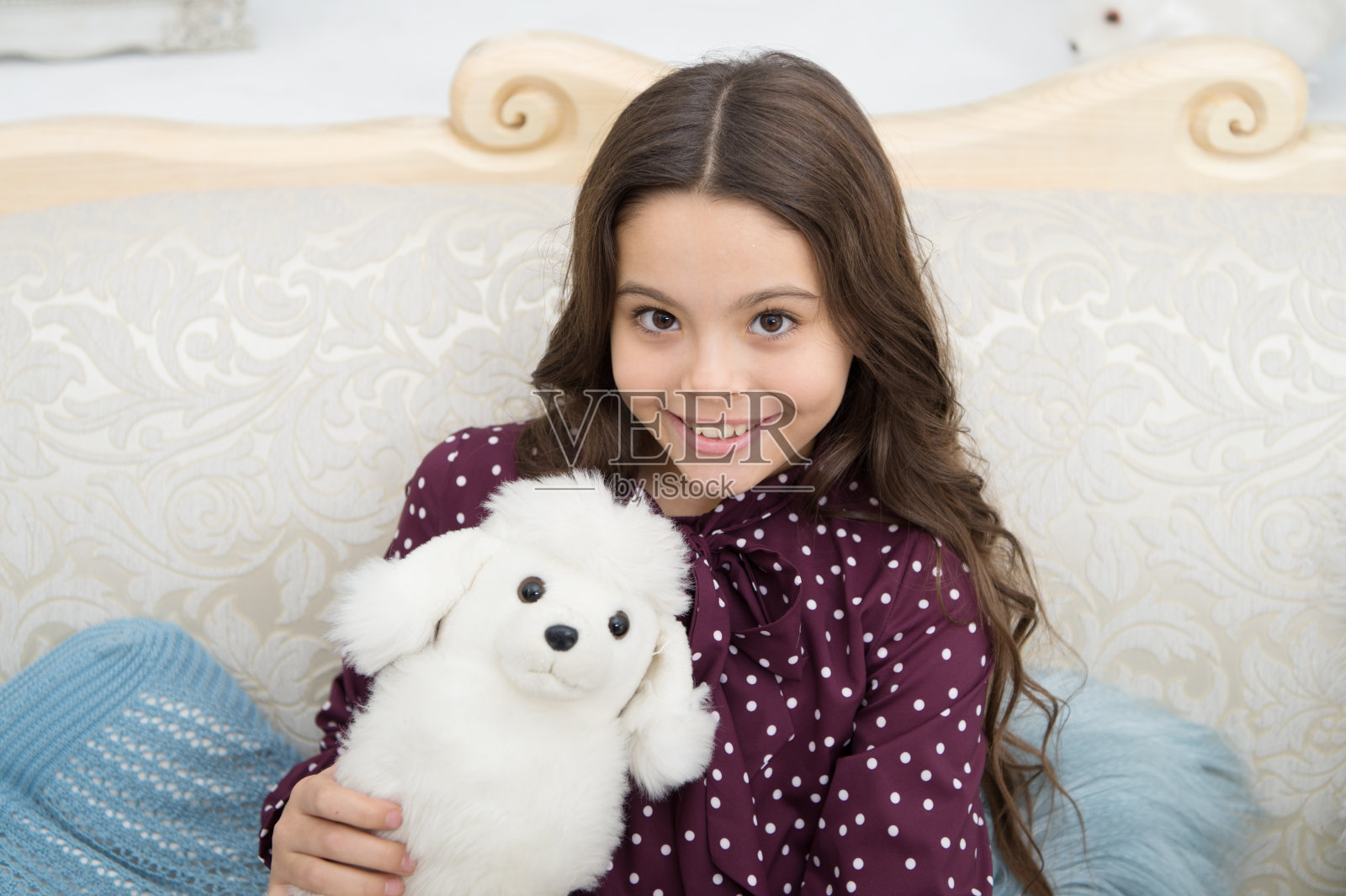 圣诞礼物的概念。孩子可爱的小女孩顽皮地抱着白色的狗毛绒玩具。小孩小女孩玩玩具狗小狗沙发背景。狗是最好的朋友。她梦到了一只真正的小狗。最喜欢的玩具照片摄影图片