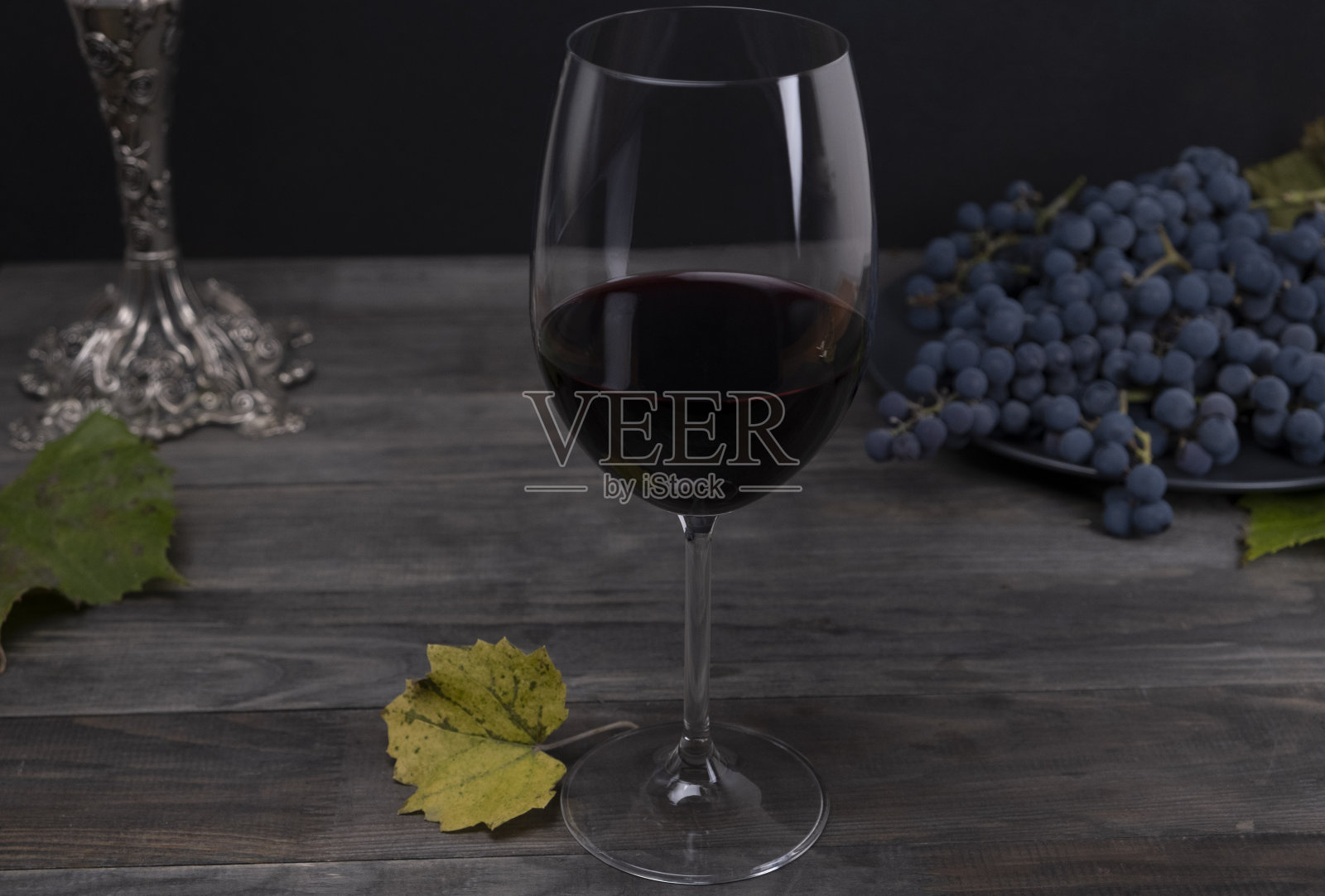 构图用一杯红酒和葡萄在深色的灰色木板背景上。酿酒的概念。静物和酒在黑暗的钥匙照片摄影图片