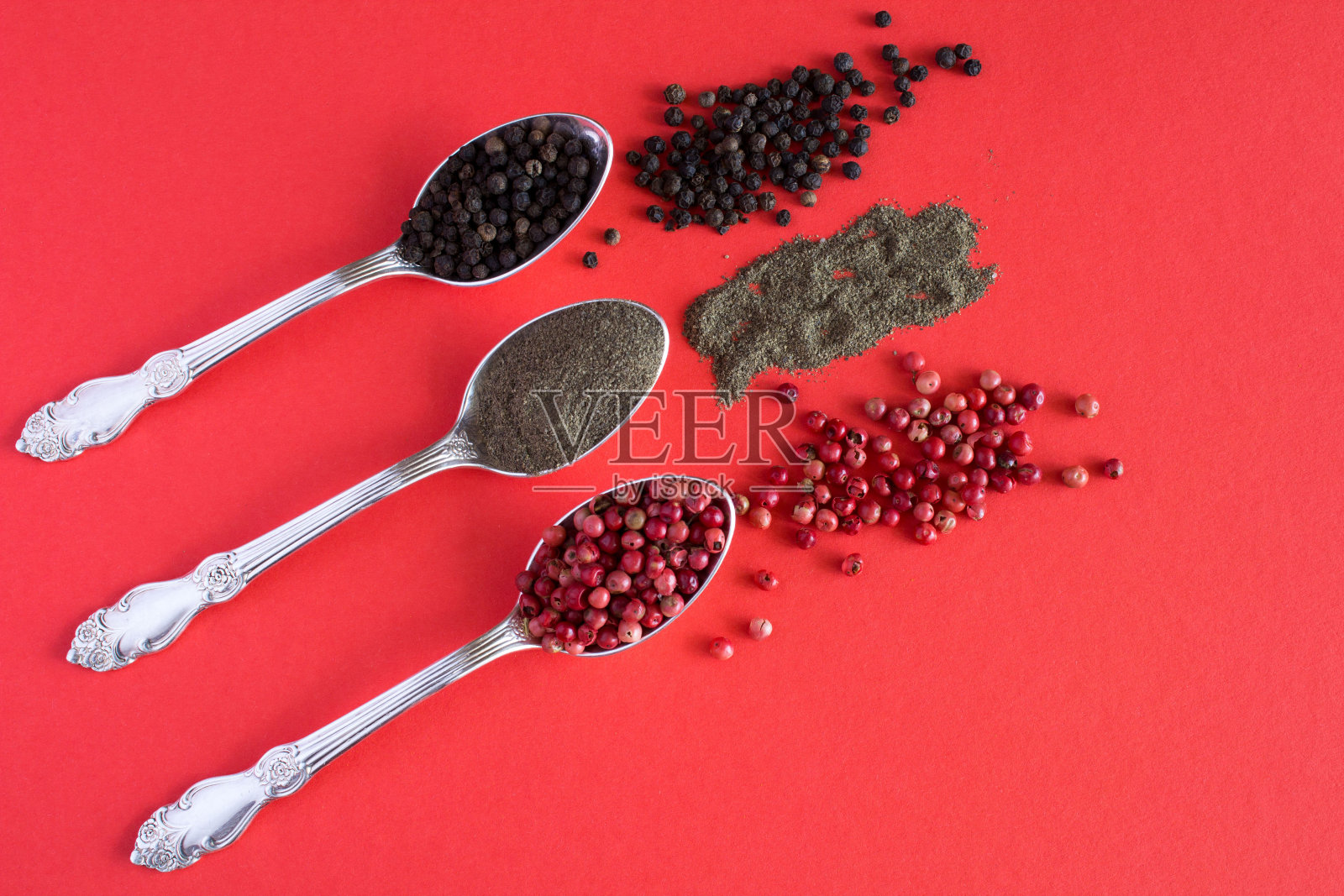 红色背景上的银勺上有红色、黑色和胡椒粉。前视图。照片摄影图片