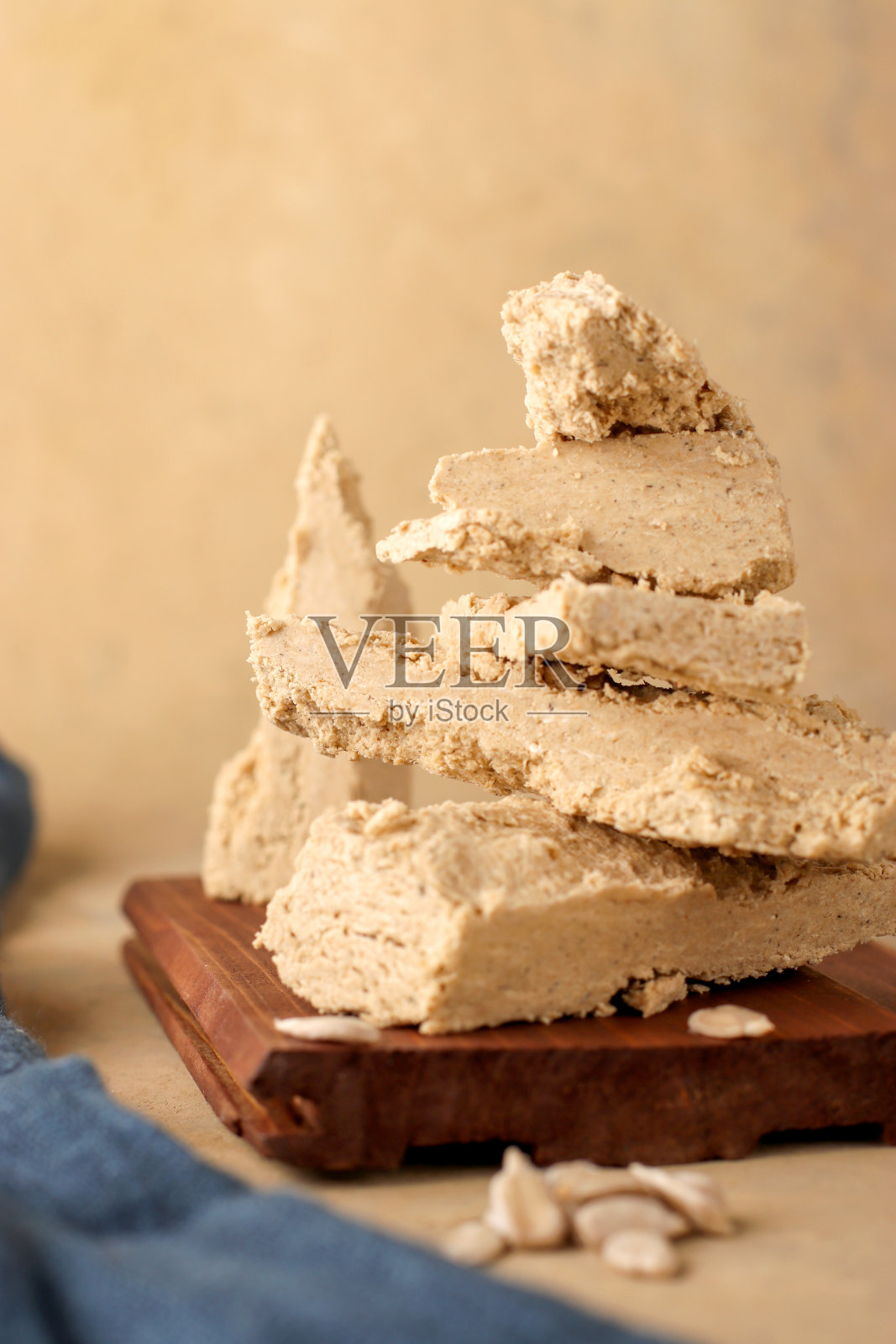 天然素食产品。向日葵halva木制板和蓝色纺织品的浅色背景。东部的甜味。乡村风格。垂直位置。照片摄影图片