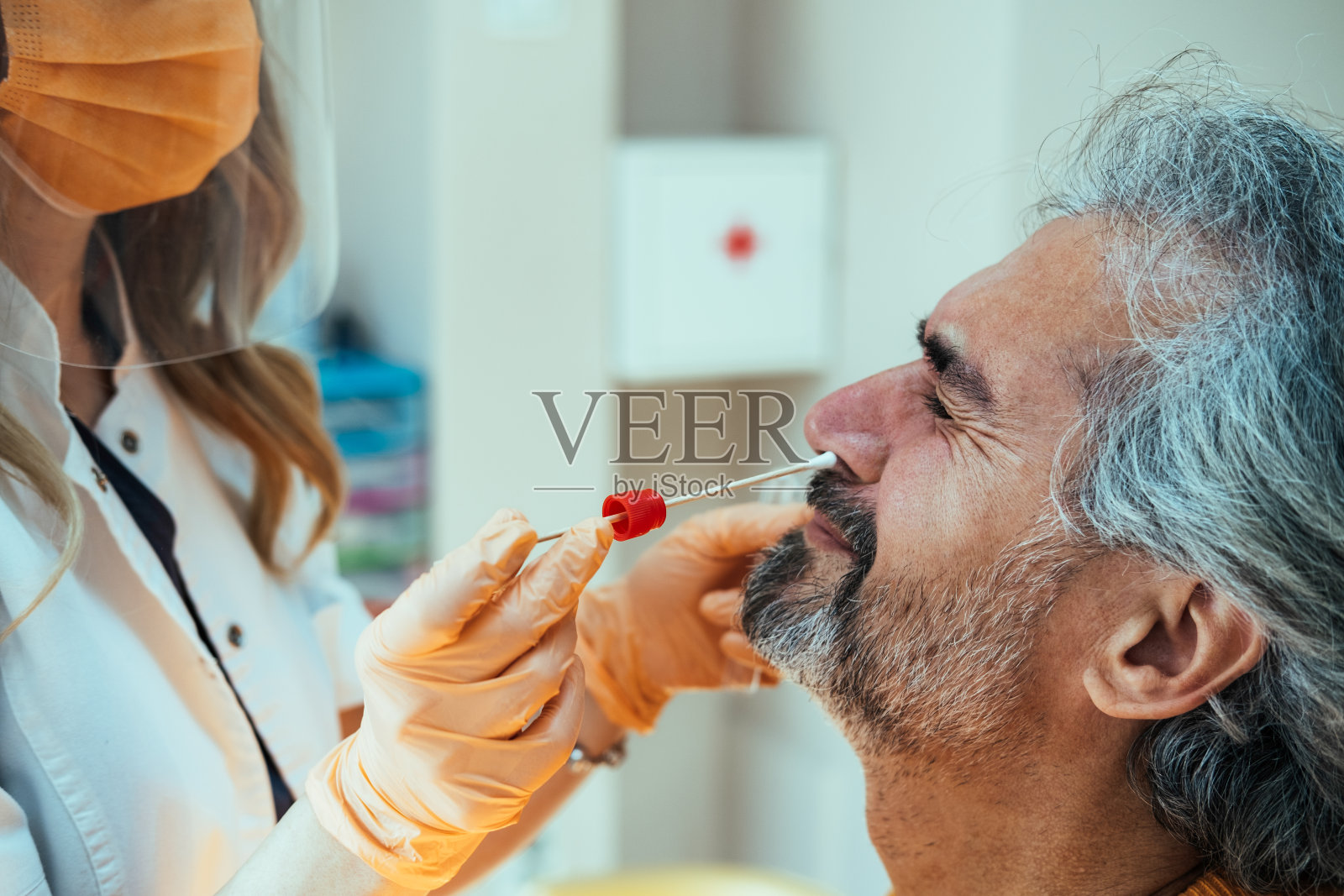 近距离拍摄的医生手戴着橙色手套，从医院的成熟男子鼻子拭子测试照片摄影图片