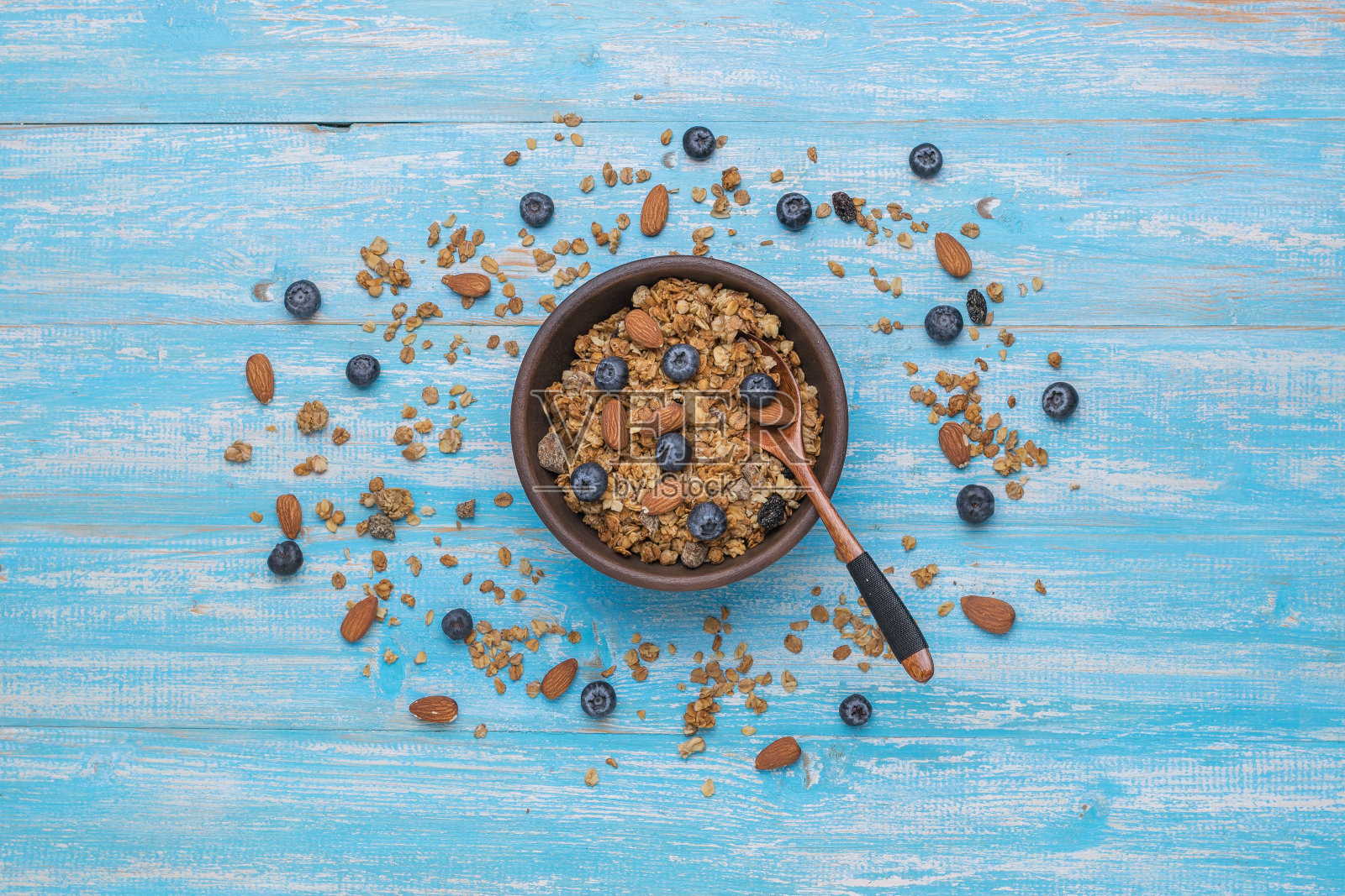 木桌上放着一个盛满坚果和蓝莓麦片的泥碗。平的。照片摄影图片