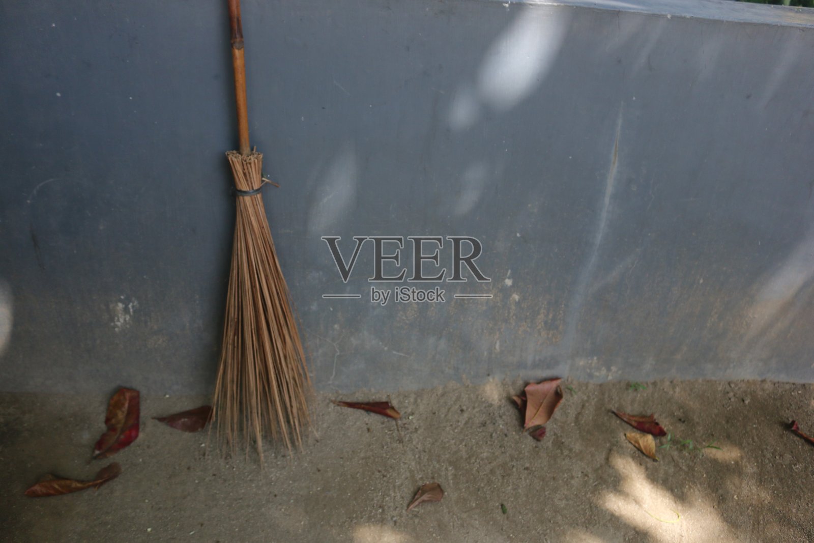 用椰叶树枝做的扫帚靠在墙上，周围有落叶照片摄影图片
