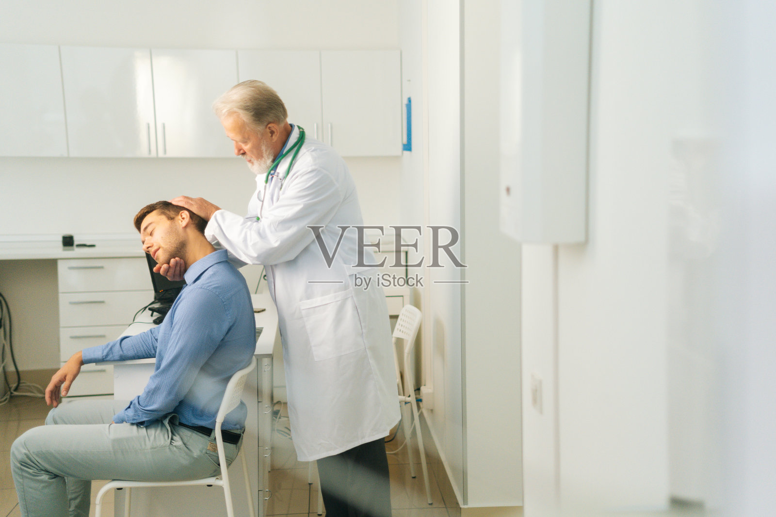 老年男性手动治疗师侧视图，转动并弯曲男性患者的头部，检查其受伤的颈部。照片摄影图片