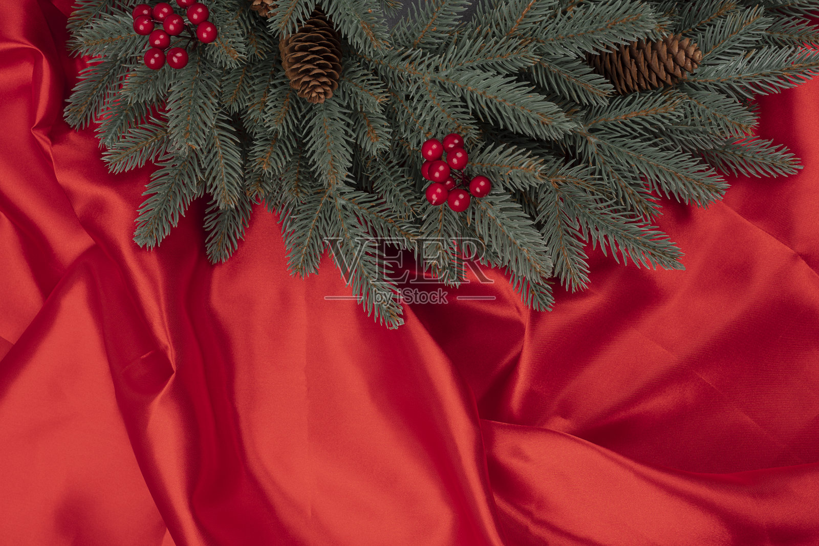 红色的冬季浆果和松果的圣诞树树枝在红色的丝绸或缎子背景上照片摄影图片
