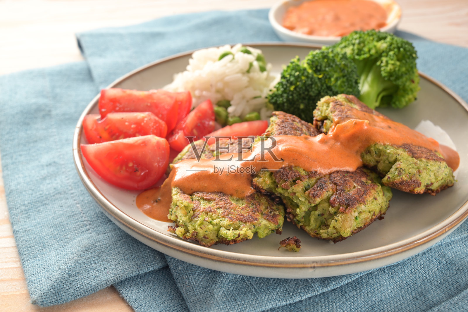 西兰花馅饼配番茄，米饭，蔬菜和辣椒酱，蓝色餐巾和浅色木桌上的素食和纯素餐，精选重点照片摄影图片