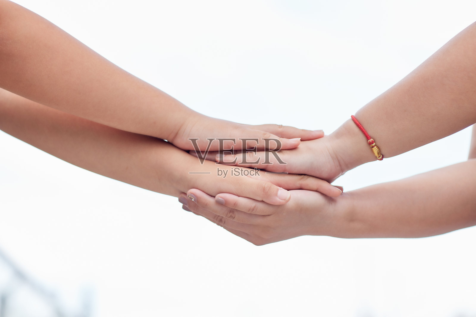 他们的双手交错堆叠在一起，背景是模糊的天空，照片摄影图片