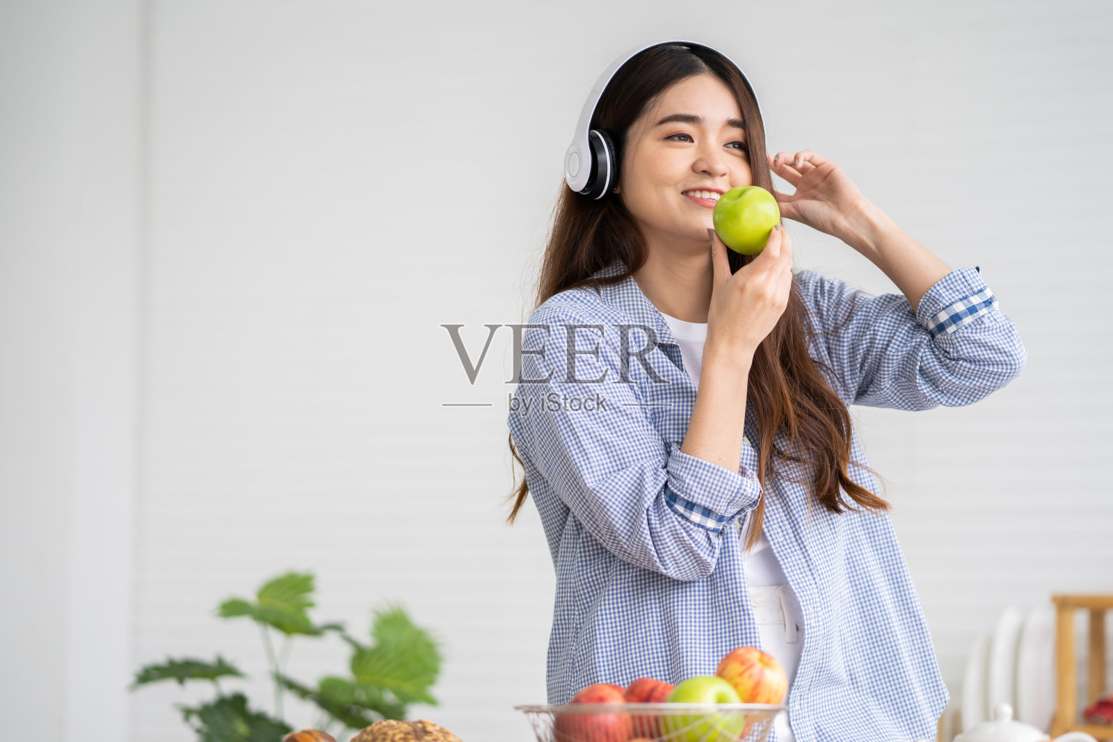 年轻的亚洲女性穿着休闲的衣服，在厨房里选择新鲜的苹果水果作为早餐。良好的营养饮食人体状况。照片摄影图片