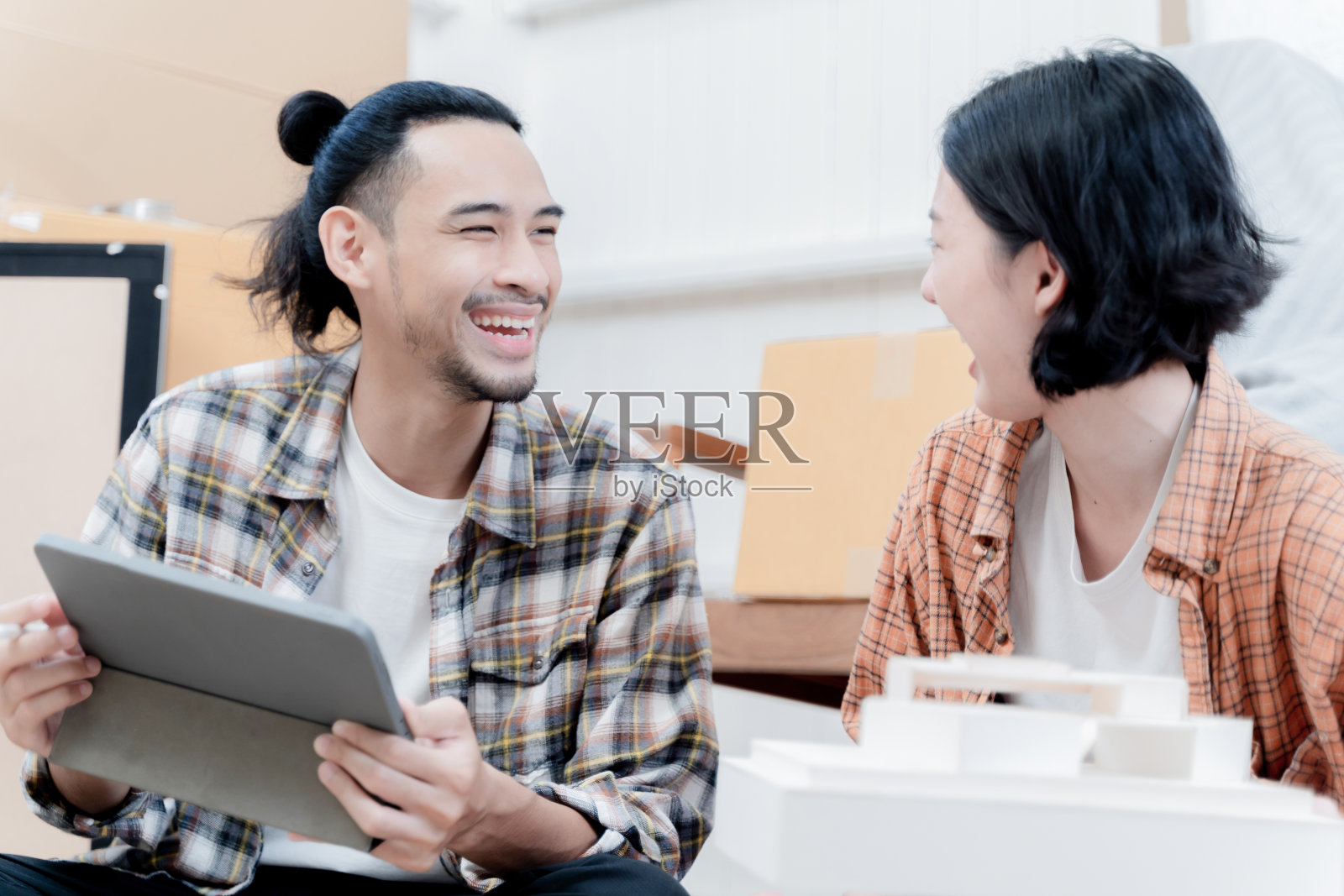 一对年轻夫妇准备装修家里的室内环境。男人在平板上画画，女人在看建筑模型。探讨客厅室内设计的新思路。照片摄影图片