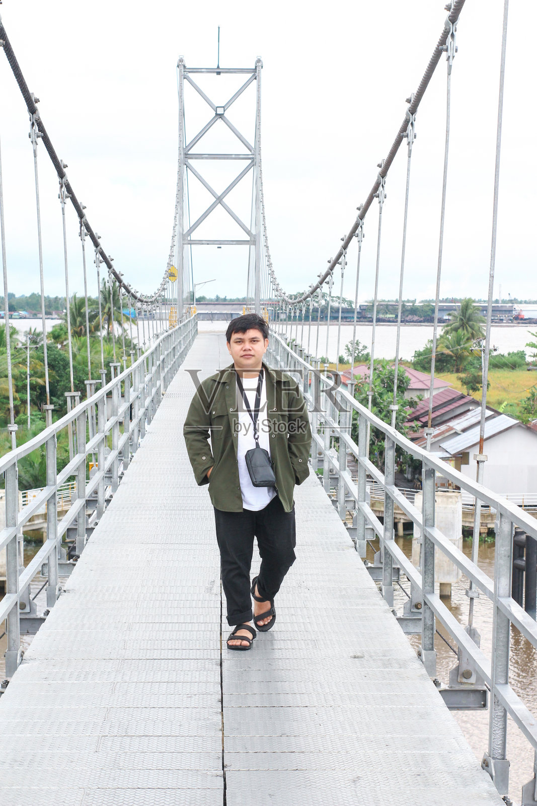 一个穿着绿色夹克的年轻人在村里的一座桥上慢慢地走着照片摄影图片