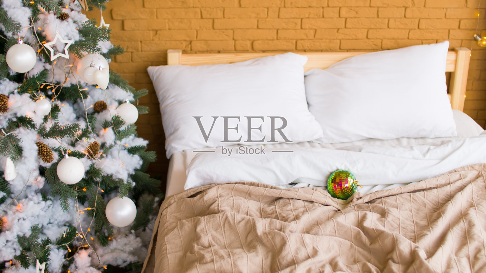 房间里床的旁边有一棵圣诞树，上面放着不同的圣诞玩具。用白色和银色的装饰品装饰针叶树，在节日期间在室内创造节日气氛照片摄影图片