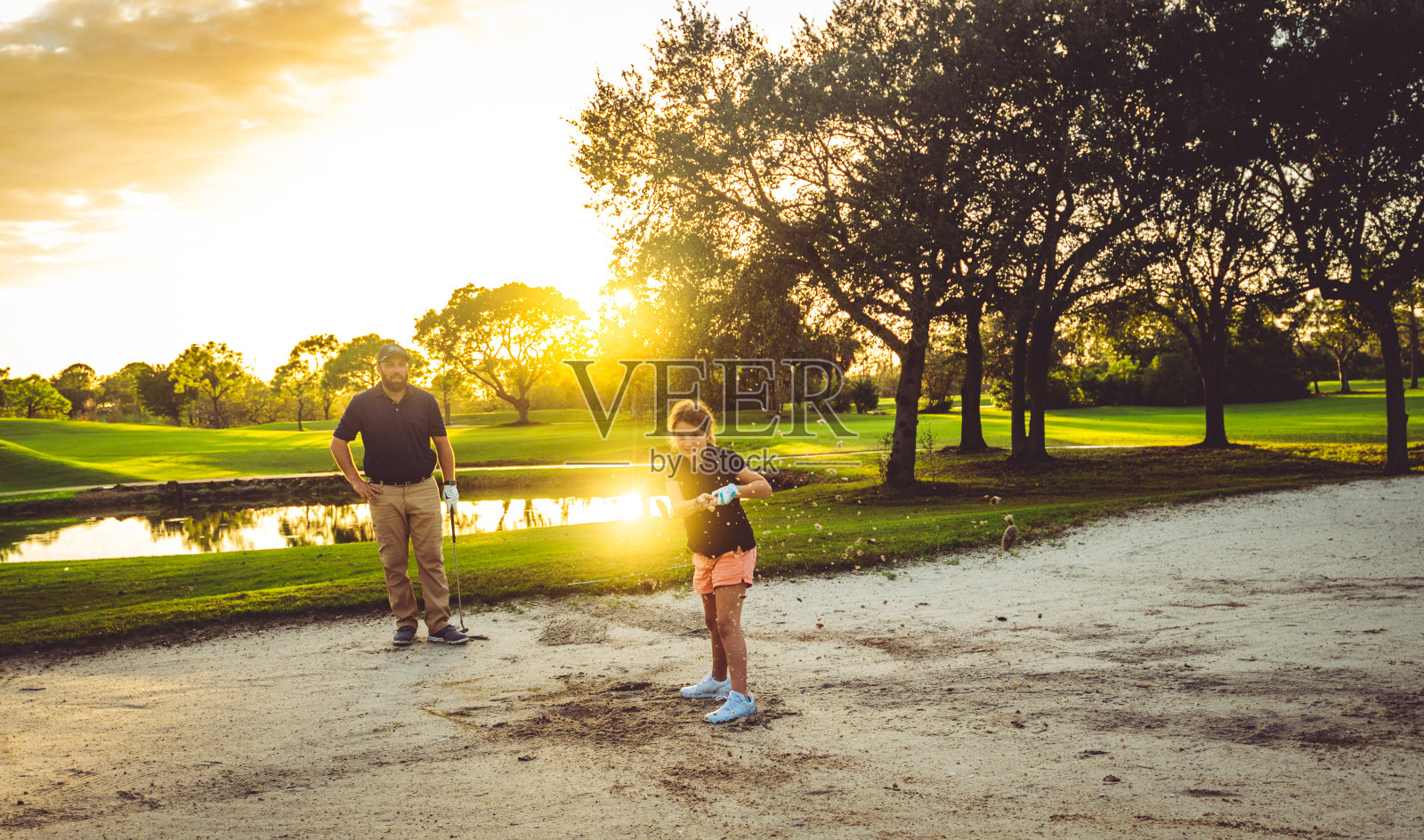 男人和女孩，父亲和女儿一起在风景优美的高尔夫球场的沙坑里打高尔夫球照片摄影图片