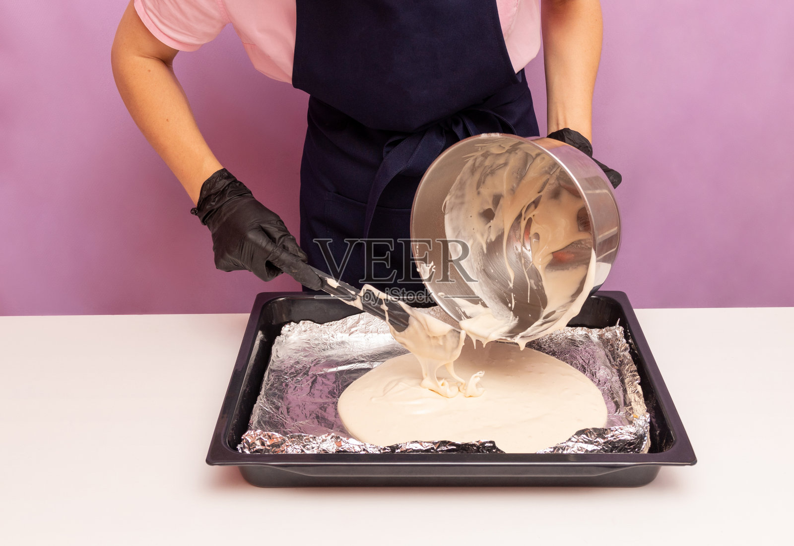 女士手戴手套，在烘烤前用抹刀将面团从碗中抹到带锡箔的烤盘上。广告食谱。有选择性的重点。照片摄影图片