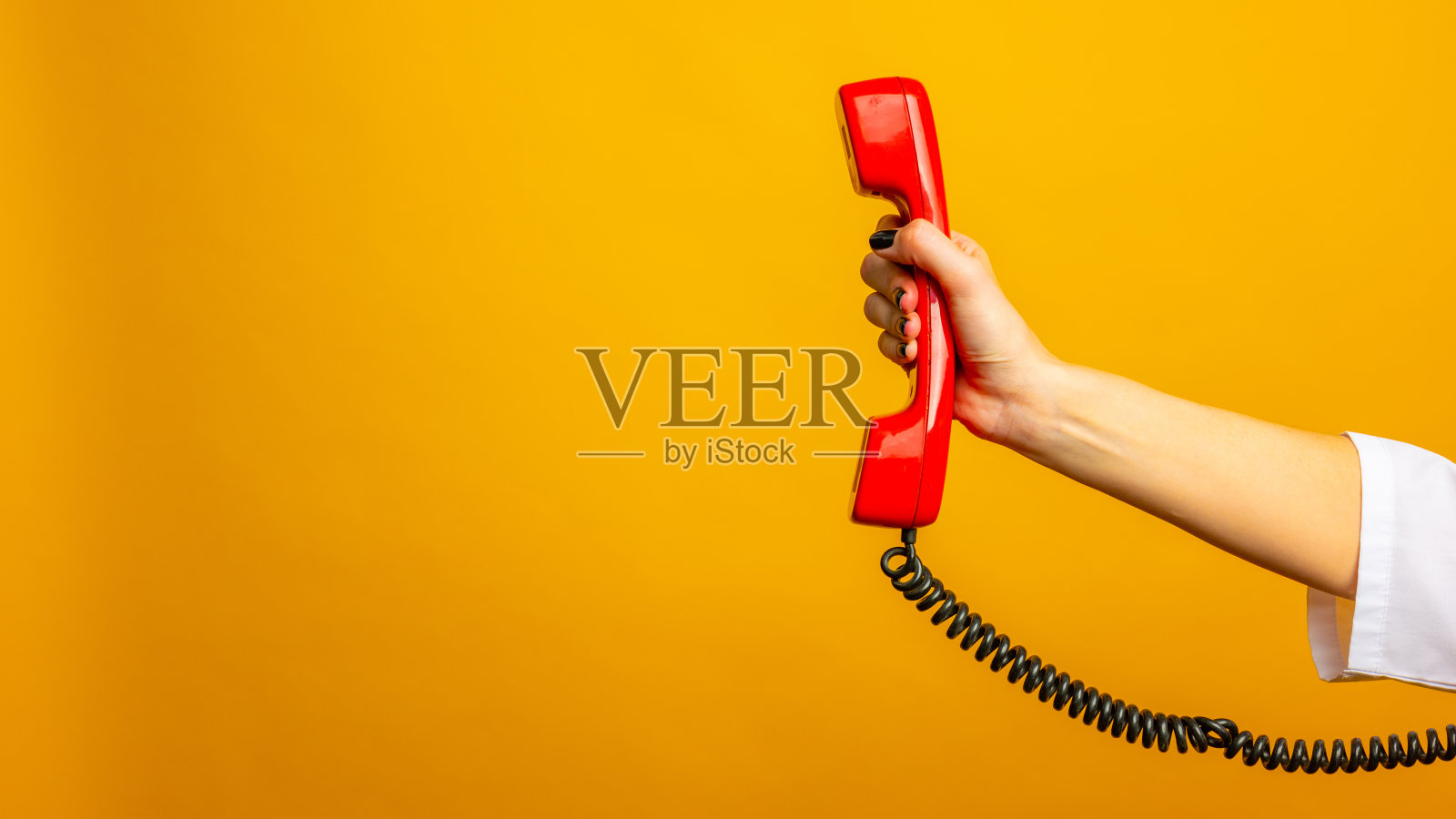 黄色背景下手持红线电话的女人特写，文字空间。热线的概念照片摄影图片