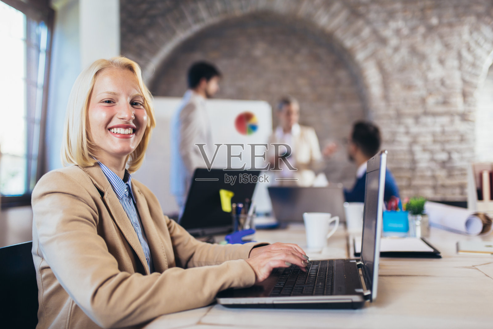 快乐的女商人使用笔记本电脑与团队讨论项目在后台。照片摄影图片