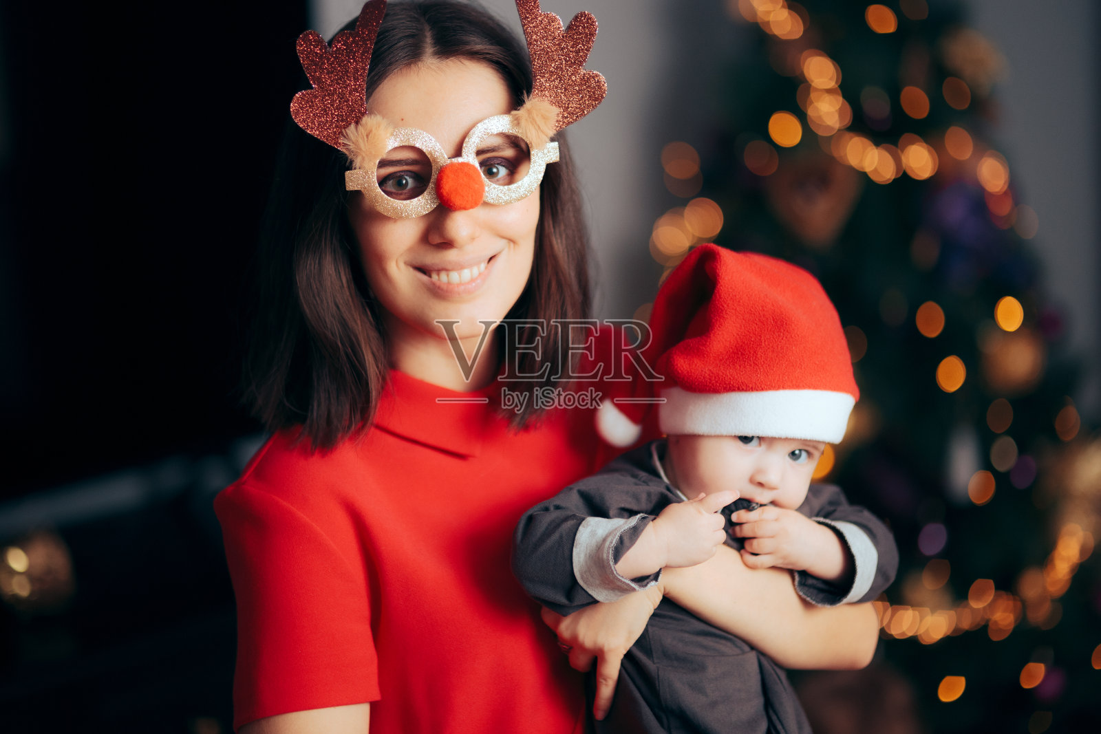 妈妈戴着滑稽的眼镜抱着她的宝宝庆祝圣诞节照片摄影图片