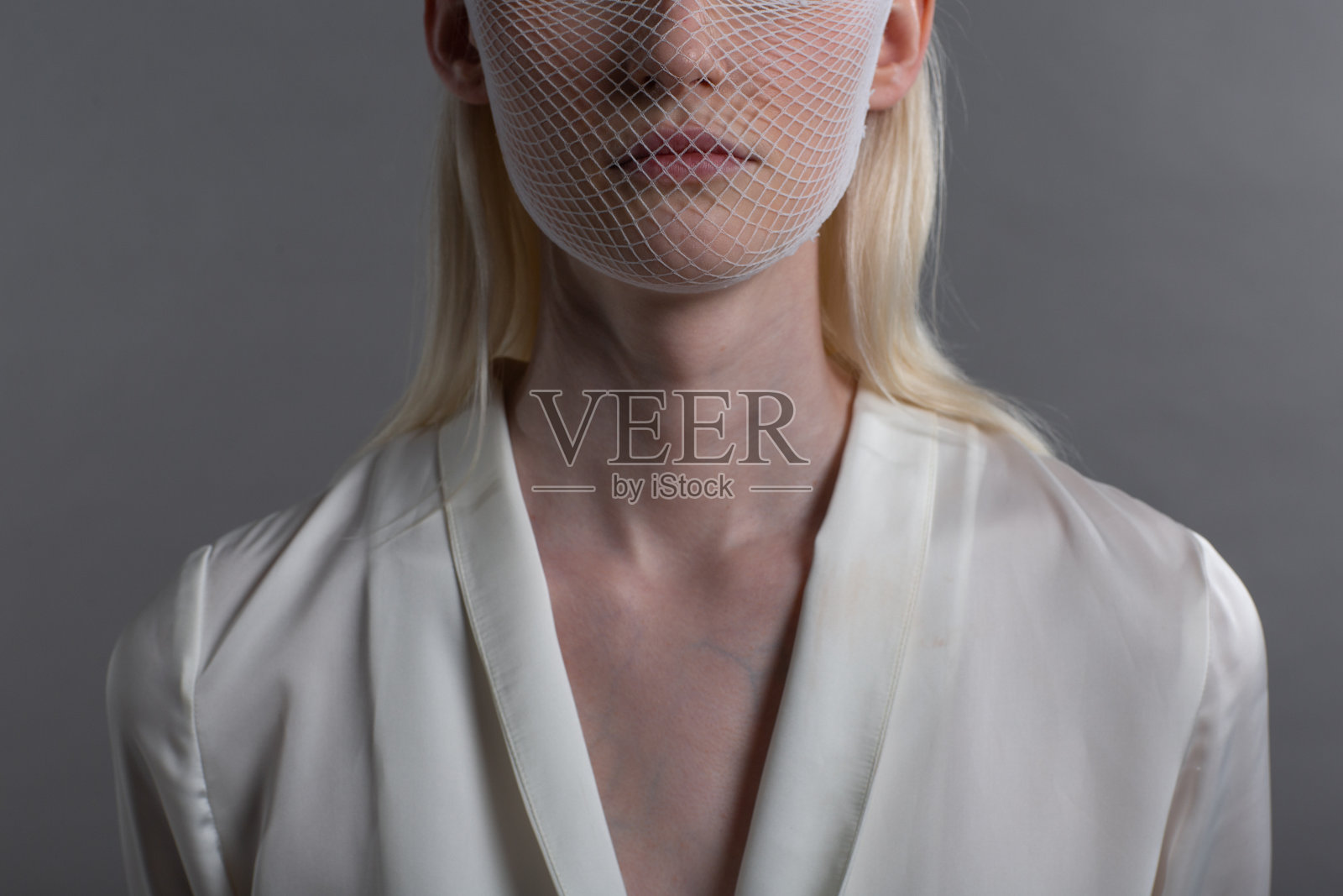 特写肖像白种人白化金发女人时装模特穿着检疫医学口罩粗网网在灰色的背景。新型冠状病毒防护理念照片摄影图片
