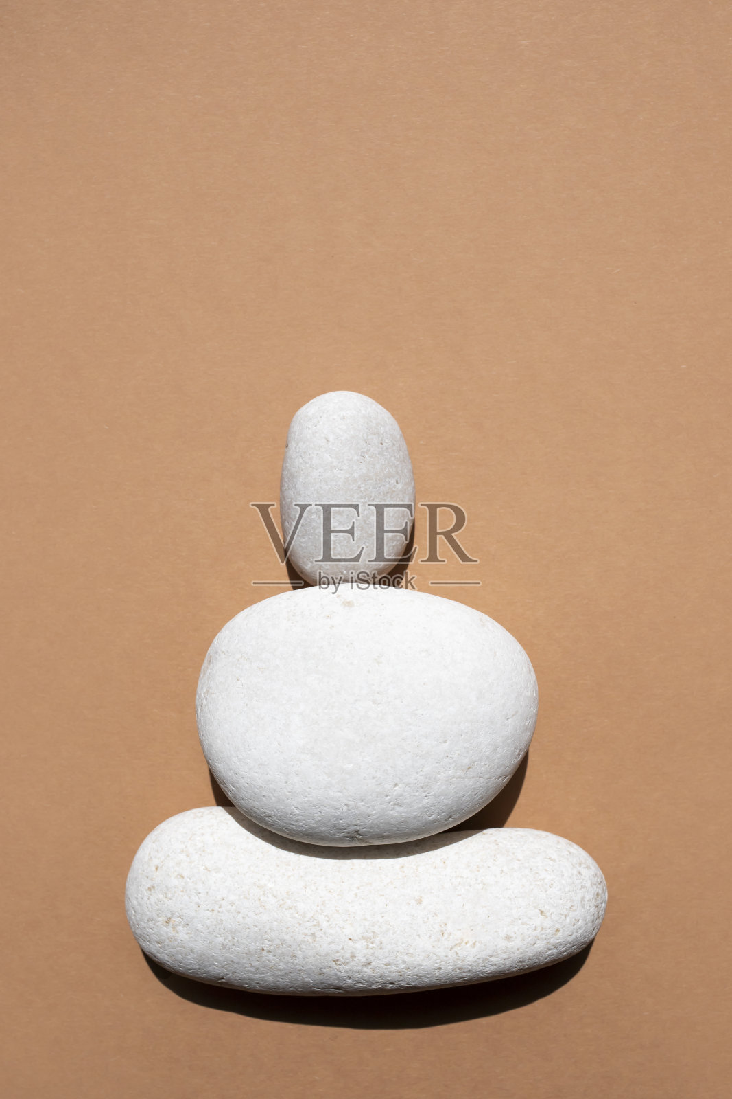 三颗白色光滑的石头在米黄色的背景上互相叠在一起。俯视图，放置文本。垂直的图像。照片摄影图片