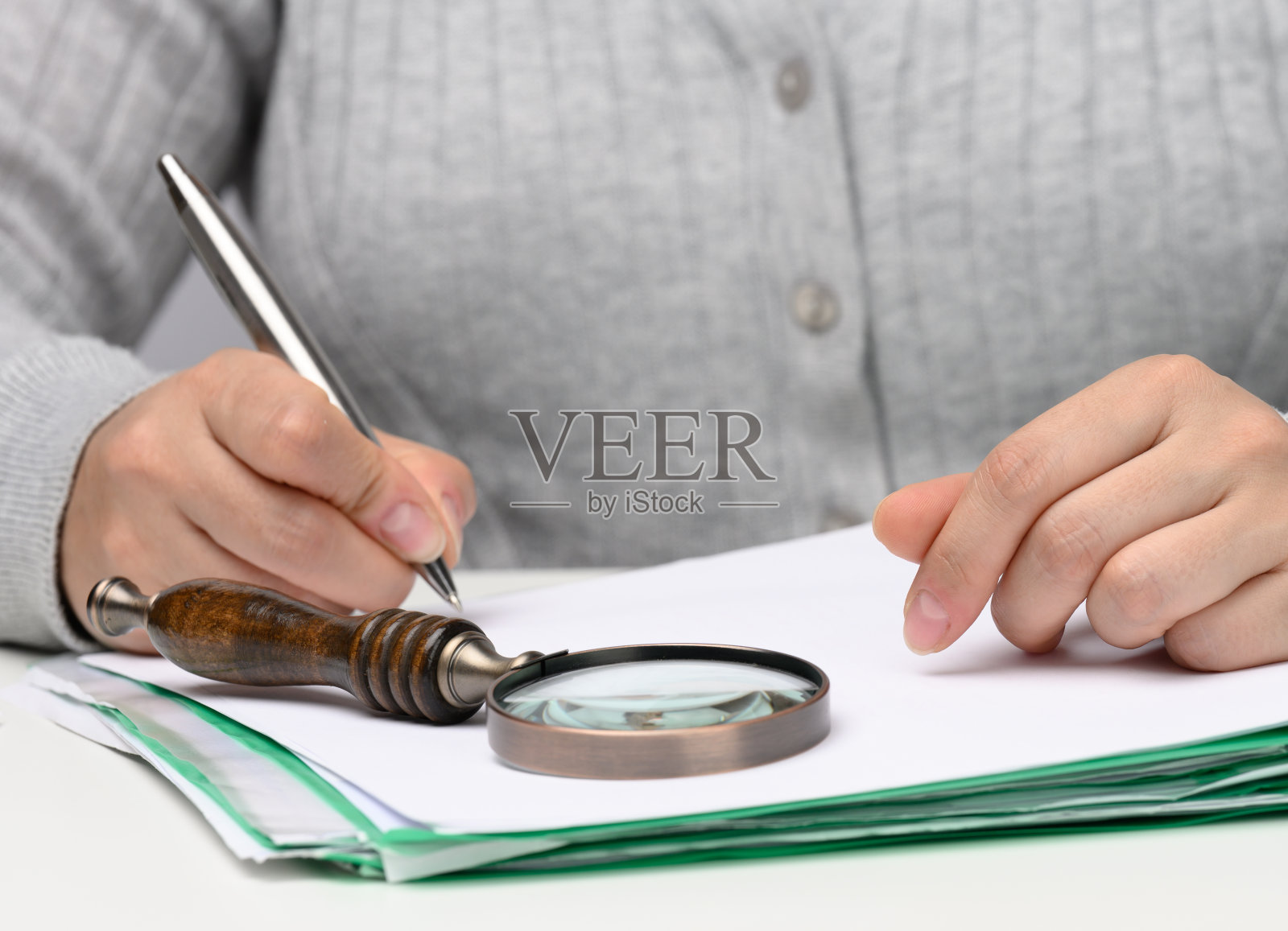 一位身穿灰色衣服的白人妇女坐在一张白色的桌子前，用金属笔签署文件。商务人员工作，签署合同和发票照片摄影图片