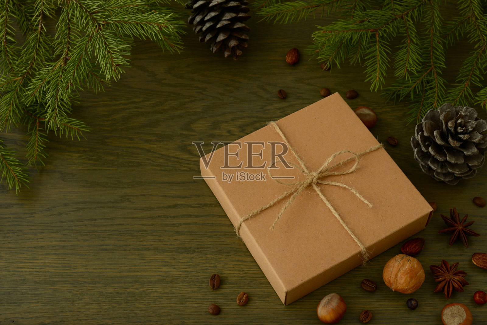 圣诞礼物在牛皮纸，锥形，坚果和圣诞树的树枝在黑暗的木制背景。节日新年或圣诞节背景，环保风格。寒假主题。空间的文本照片摄影图片