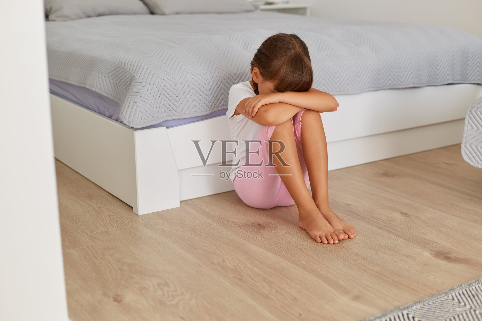 心烦意乱的小女孩独自坐在地板上哭泣，坐在床边低下头，悲伤孤独的孩子被欺负虐待，感到压力或害怕，儿童暴力。照片摄影图片