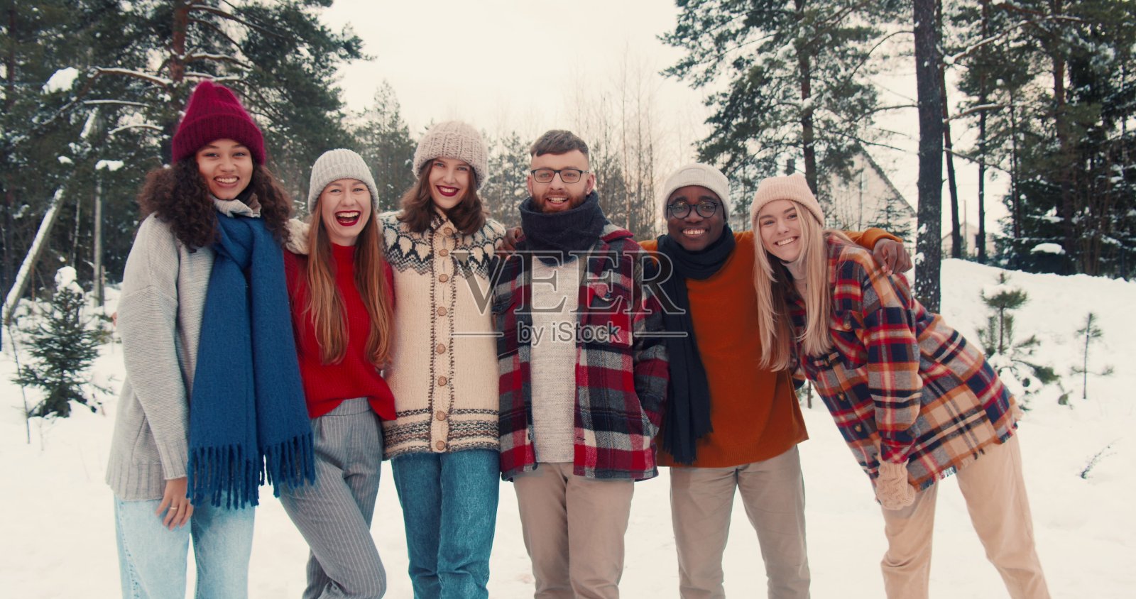 团结的概念。快乐的多民族朋友看着镜头，在雪林慢动作中展示爱心手势。照片摄影图片