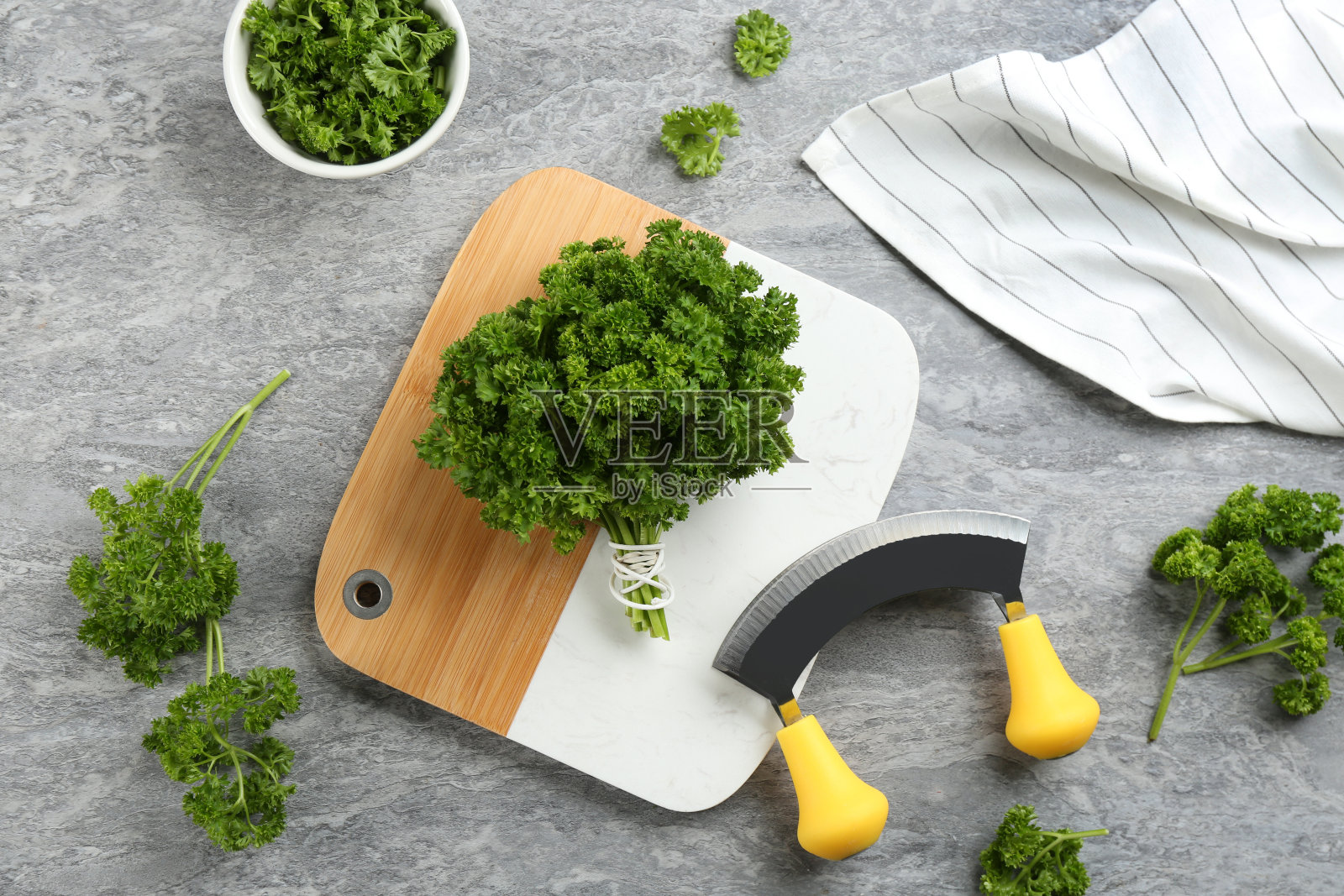 新鲜卷曲的欧芹，切菜板和切碎刀放在灰色的桌子上，平铺照片摄影图片
