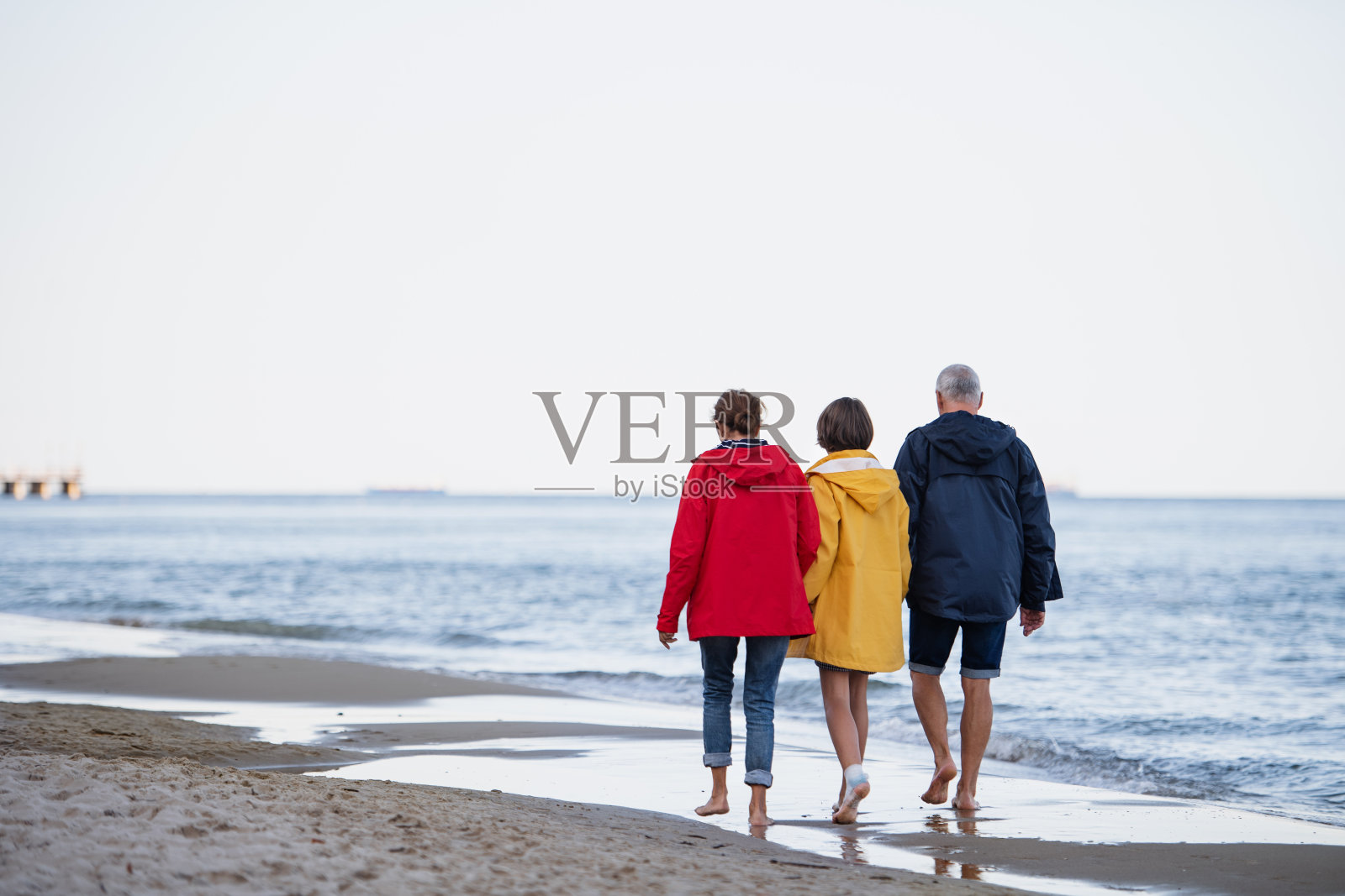 后视镜:老年夫妇牵着他们不到十岁的孙女在沙滩上散步照片摄影图片