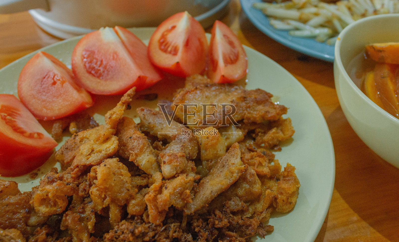 酥脆的猪肉在油里炸，西红柿切成方块。把它放在盘子里照片摄影图片