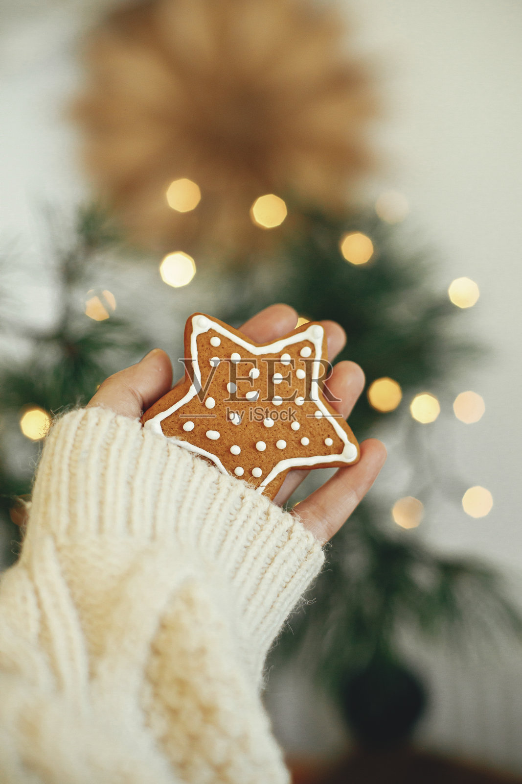 手在舒适的毛衣拿姜饼饼干星穆迪背景与灯光。节日快乐照片摄影图片