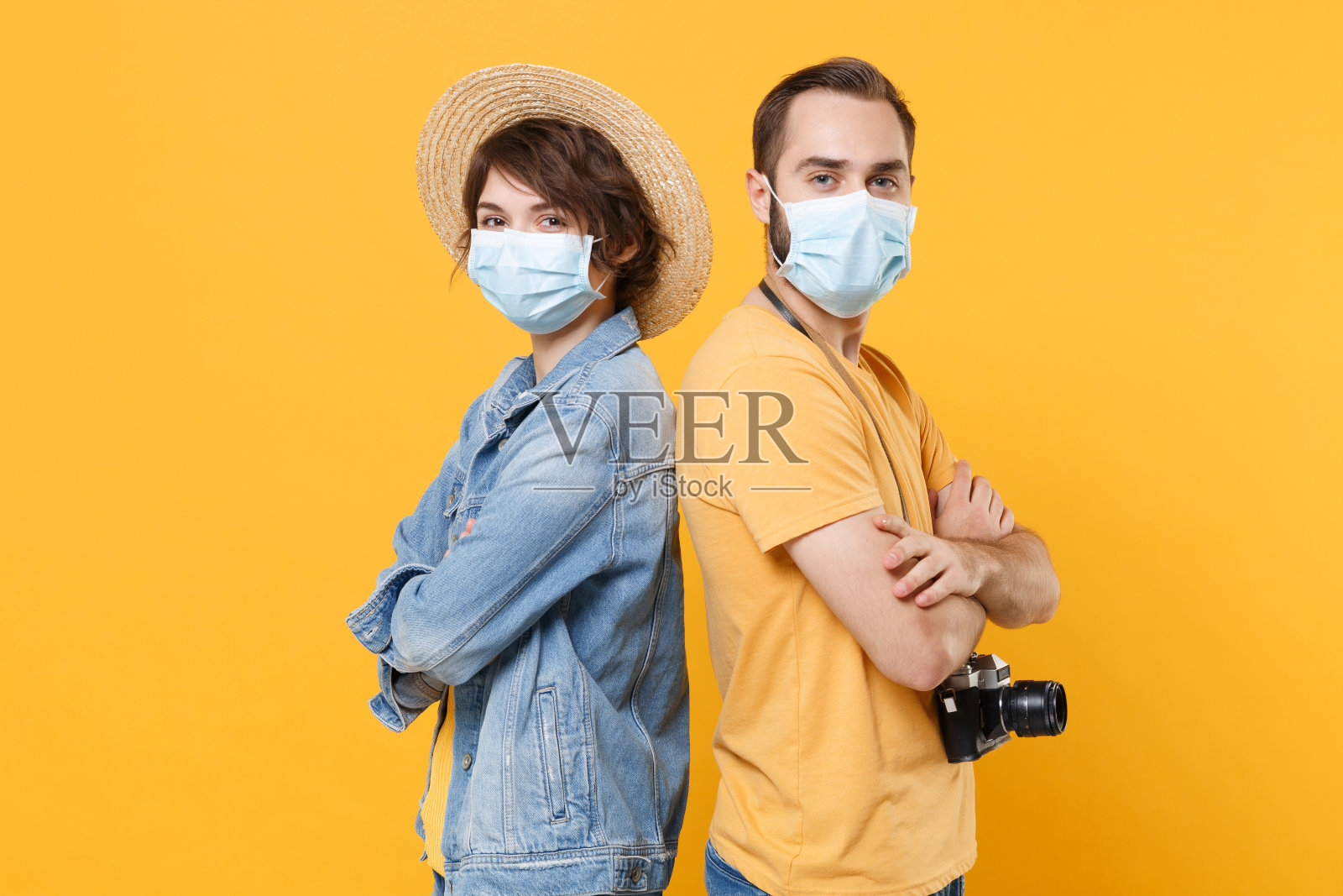 年轻的游客夫妇两个朋友男孩女孩戴着无菌口罩隔离在黄色背景上。冠状病毒2019-ncov sars covid-19流感病毒概念。背靠背站着。照片摄影图片
