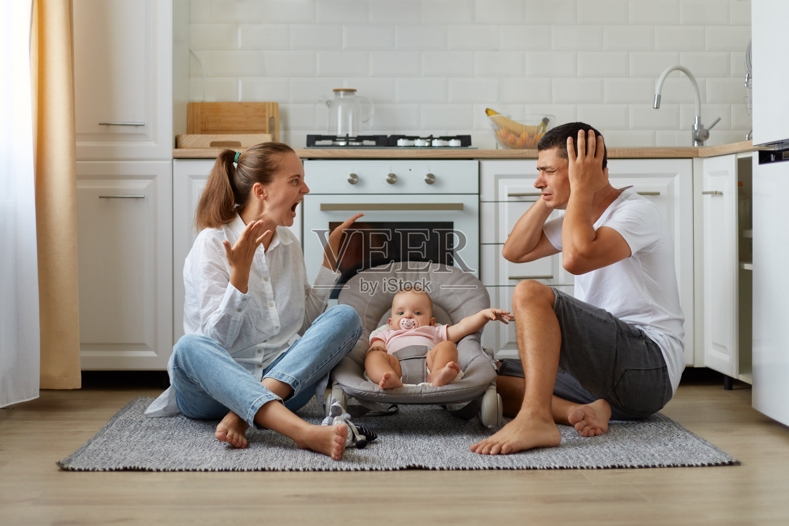 室内除了夫妻俩坐在厨房地板上争吵，妻子大声尖叫，丈夫用手掌捂住耳朵，一家人抱着婴儿在摇椅上摆姿势。照片摄影图片