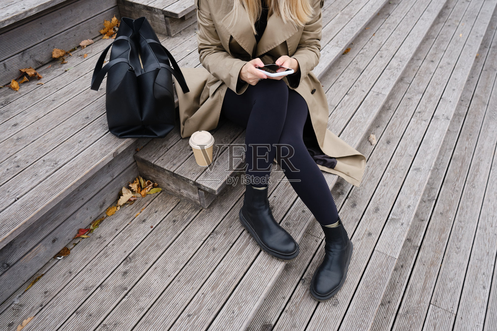 时尚的女商人坐在街上的楼梯上发短信或使用手机上的应用程序。一个手里拿着智能手机的女孩在商务中心附近。智能手机关闭照片摄影图片