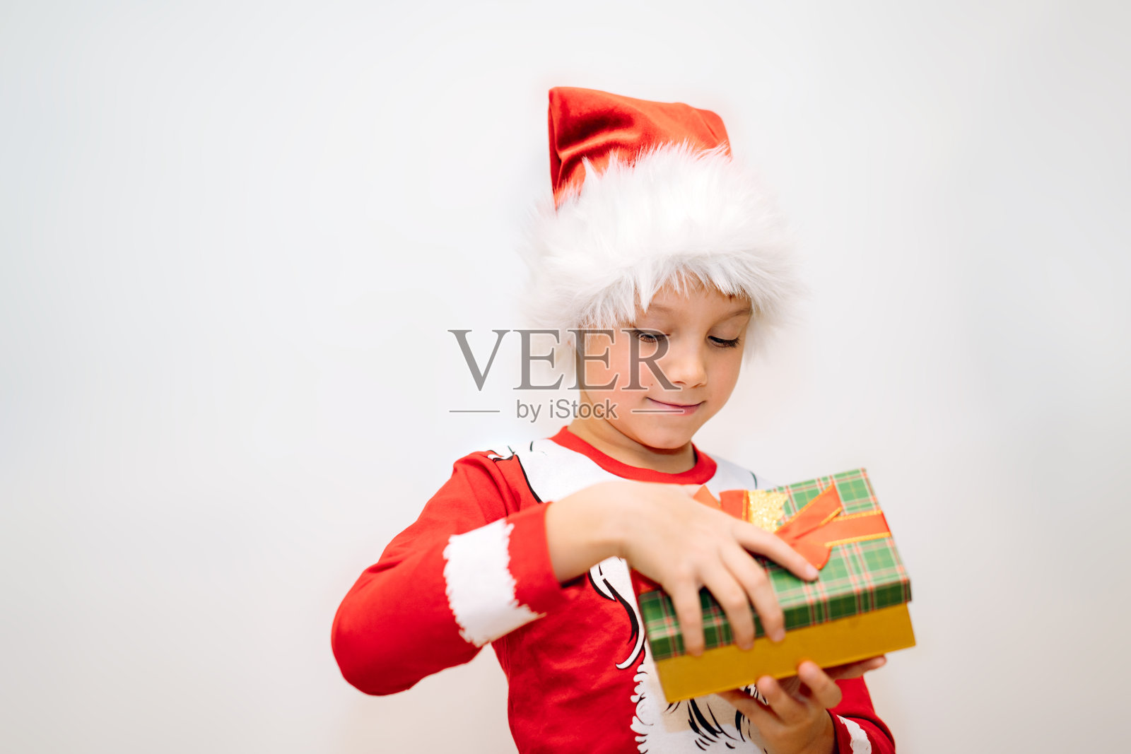 快乐微笑的白人男孩在圣诞老人t恤和帽子打开一个盒子的圣诞礼物照片摄影图片
