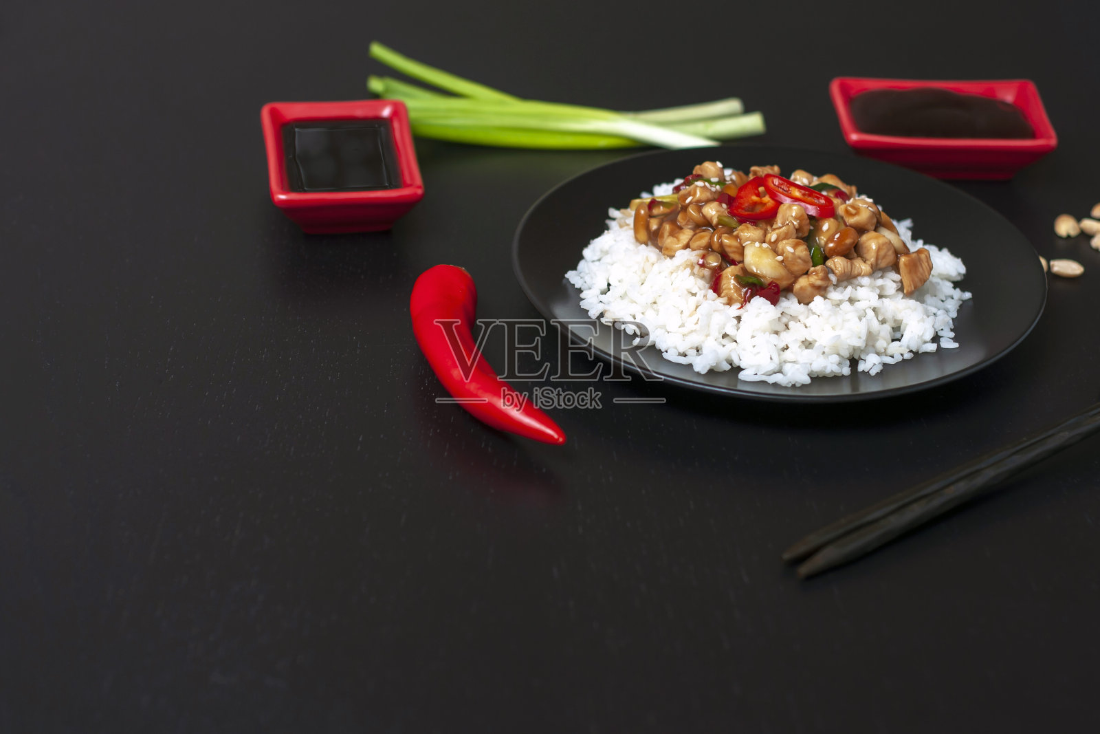宫保鸡丁和米饭放在黑色的桌子上，配上酱汁和配料。川菜一种受欢迎的中国川菜，由鸡肉、花生、辣椒、酱料和香料制成。副本的空间。照片摄影图片